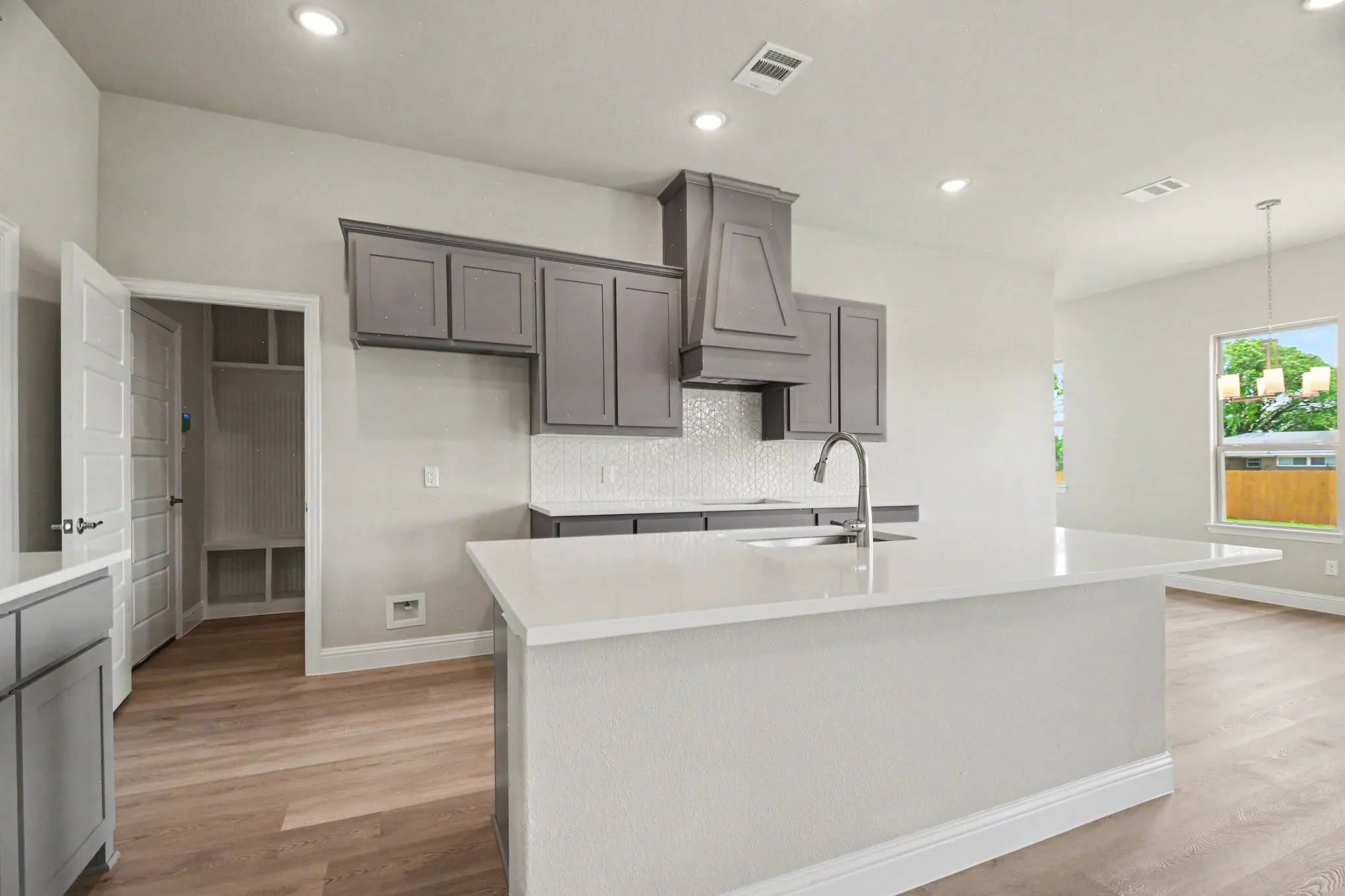 Modern kitchen featuring a large center island with a white countertop, gray cabinetry, a decorative range hood, and a white mosaic tile backsplash