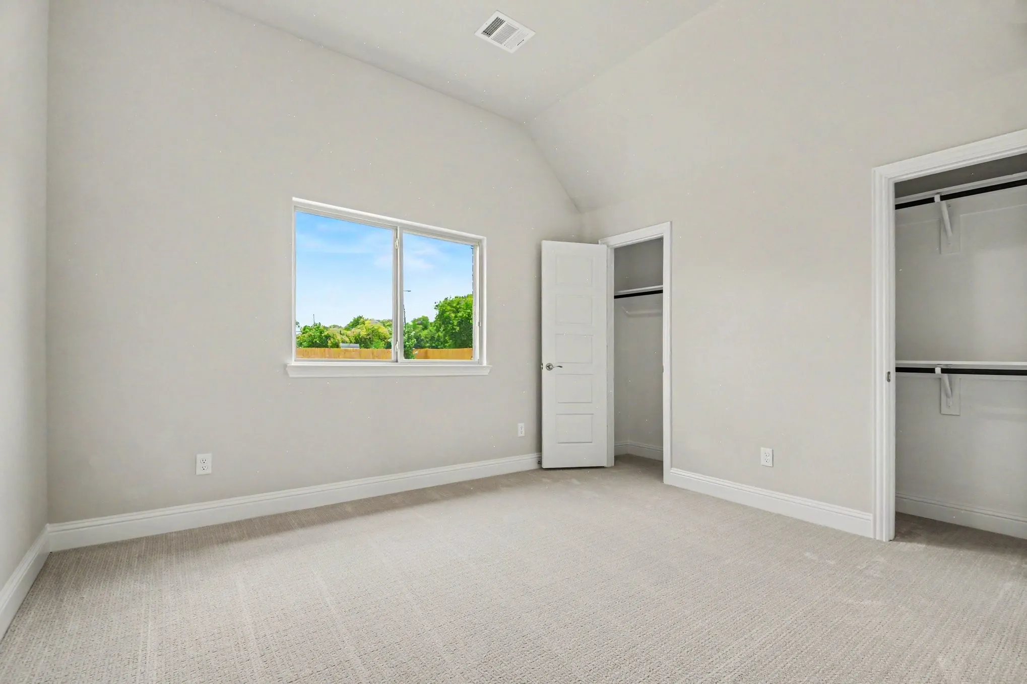 Spacious room featuring vaulted ceilings, light-colored carpeting, a large window, and two separate closets with built-in shelving and hanging rods