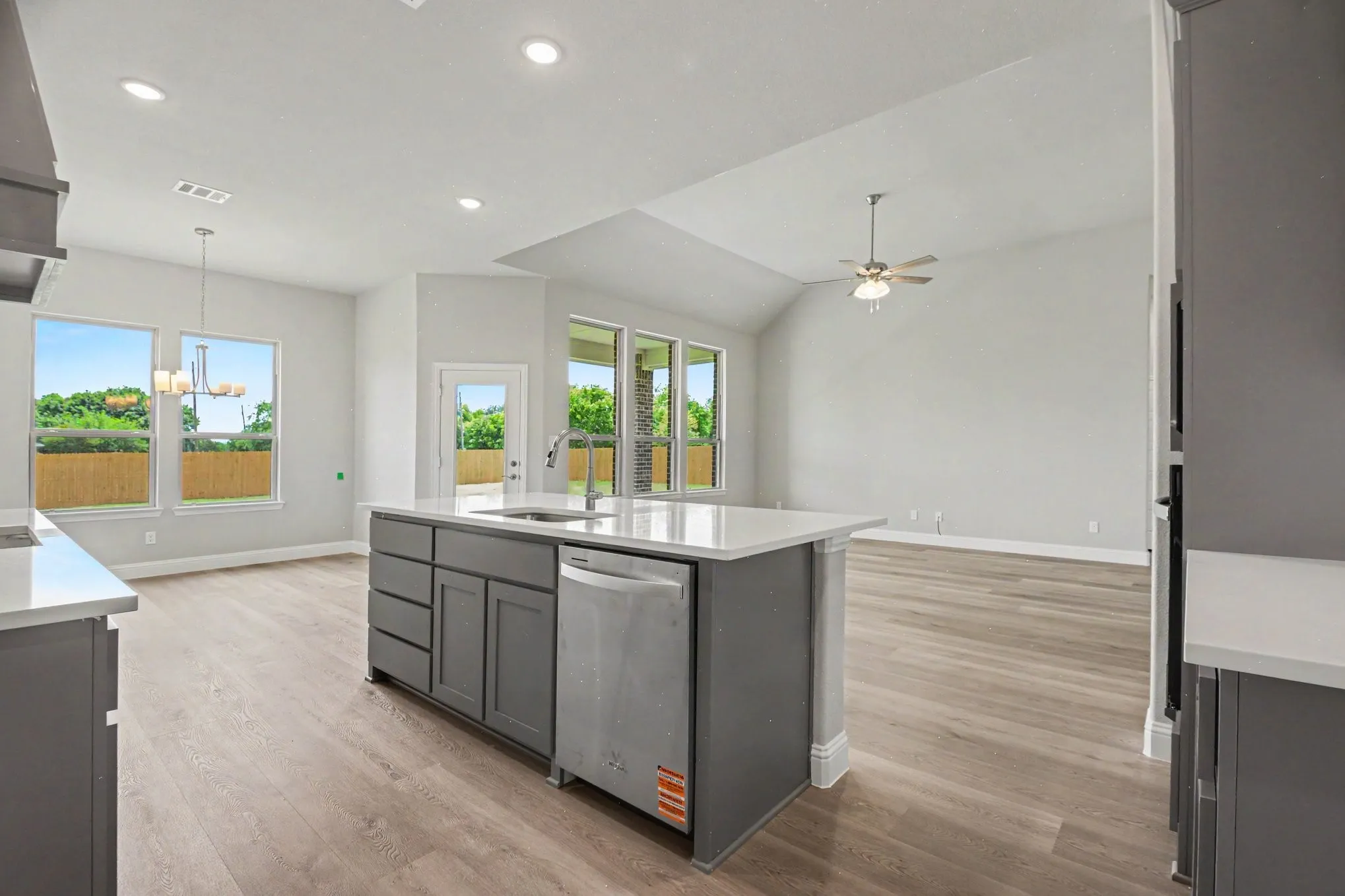Open-concept kitchen and living area featuring a central island with integrated sink and dishwasher, light-toned wood-finish flooring, recessed lighting, and a vaulted ceiling with a ceiling fan