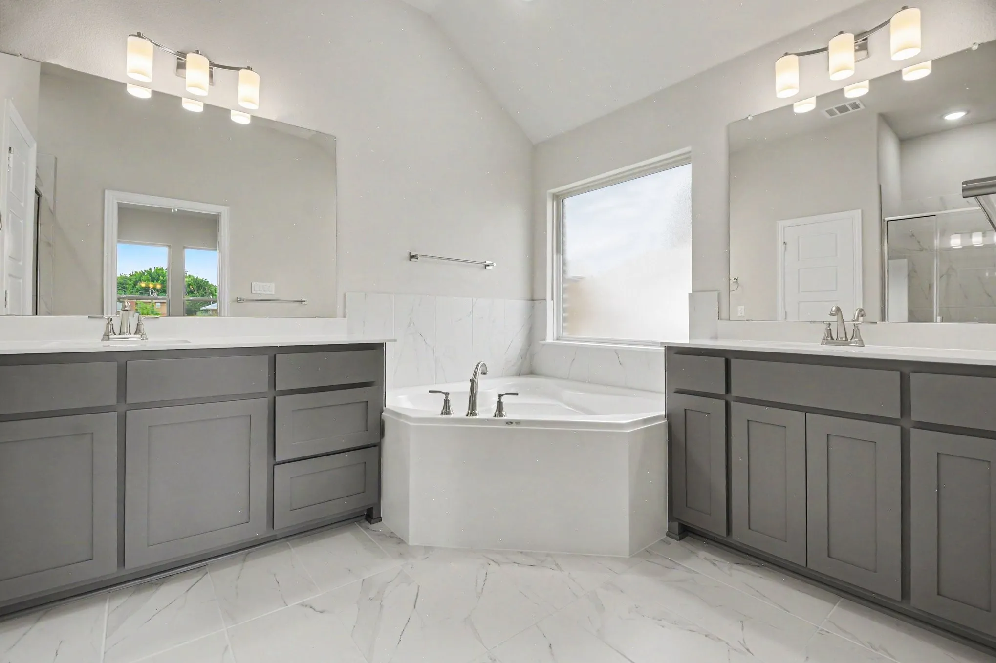 Bathroom featuring a built-in soaking tub, dual vanity sinks, extensive counter space, large wall-mounted mirrors, and tiled flooring