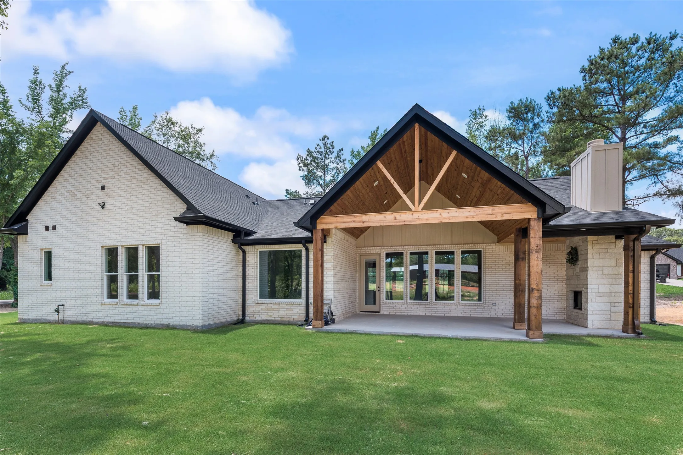 Expansive backyard featuring a manicured lawn, a covered patio with exposed wood beams, and a stone-clad outdoor fireplace