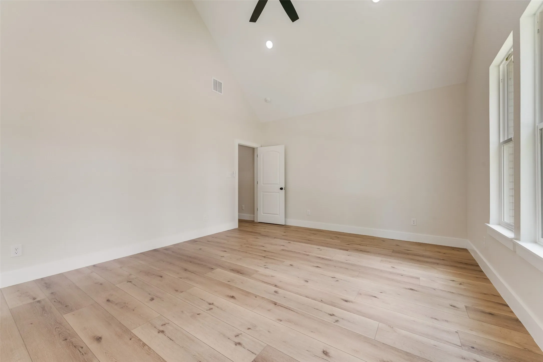 Spacious room featuring wood-finish flooring, vaulted ceilings, recessed lighting, a ceiling fan, and multiple windows