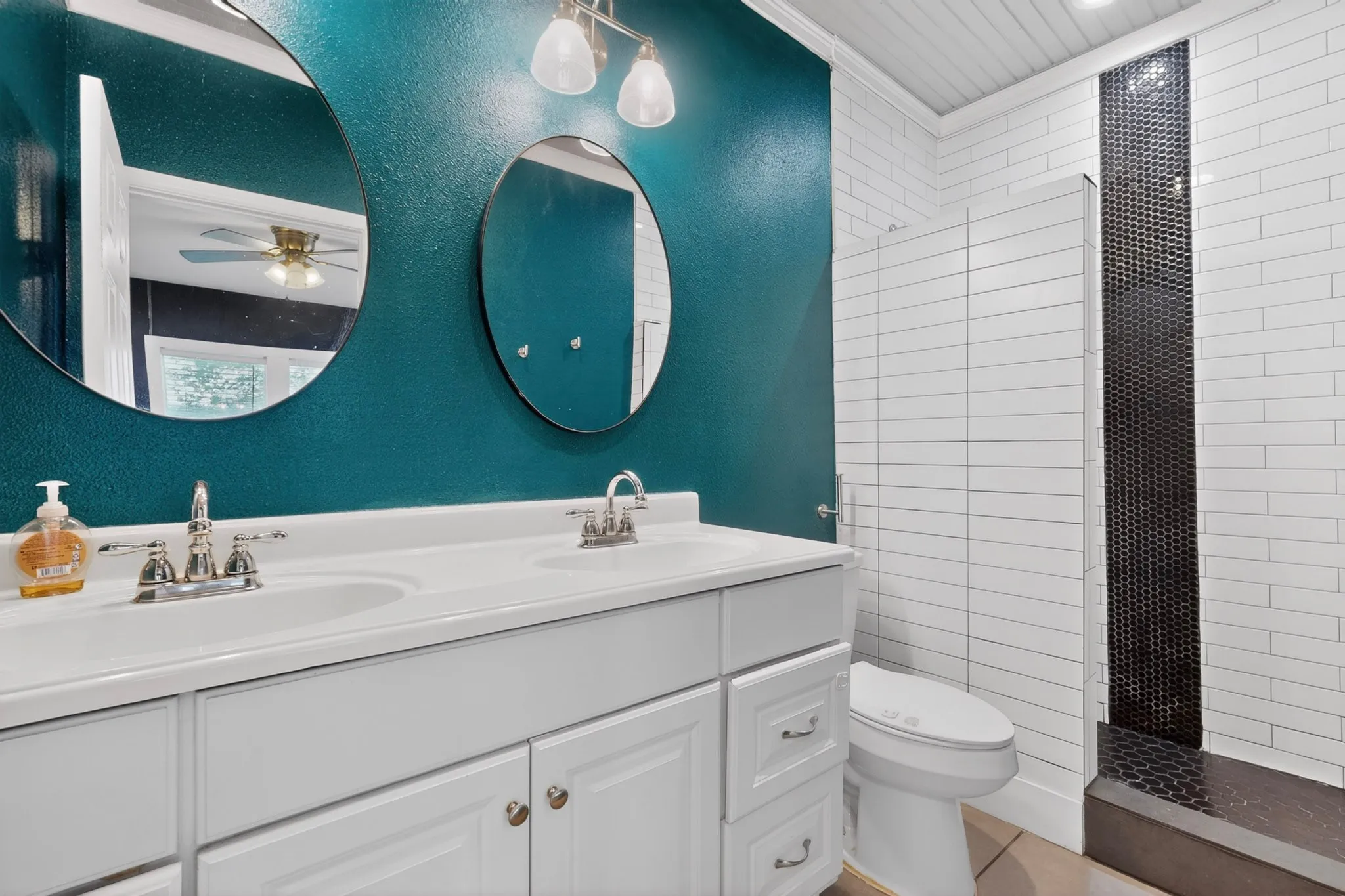 Bathroom featuring a double vanity with white cabinetry, two round mirrors, and a chrome light fixture