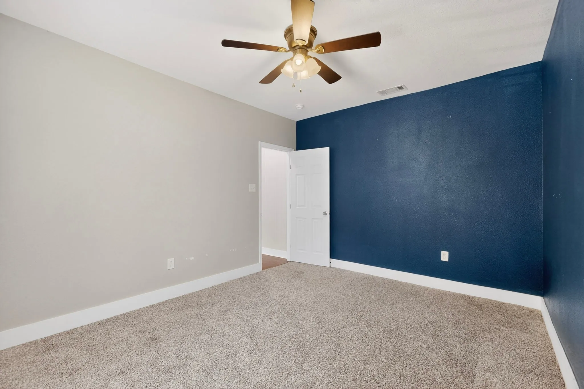 Neutral tone walls featuring an accent wall, wall-to-wall carpeting, white trim, and a ceiling fan
