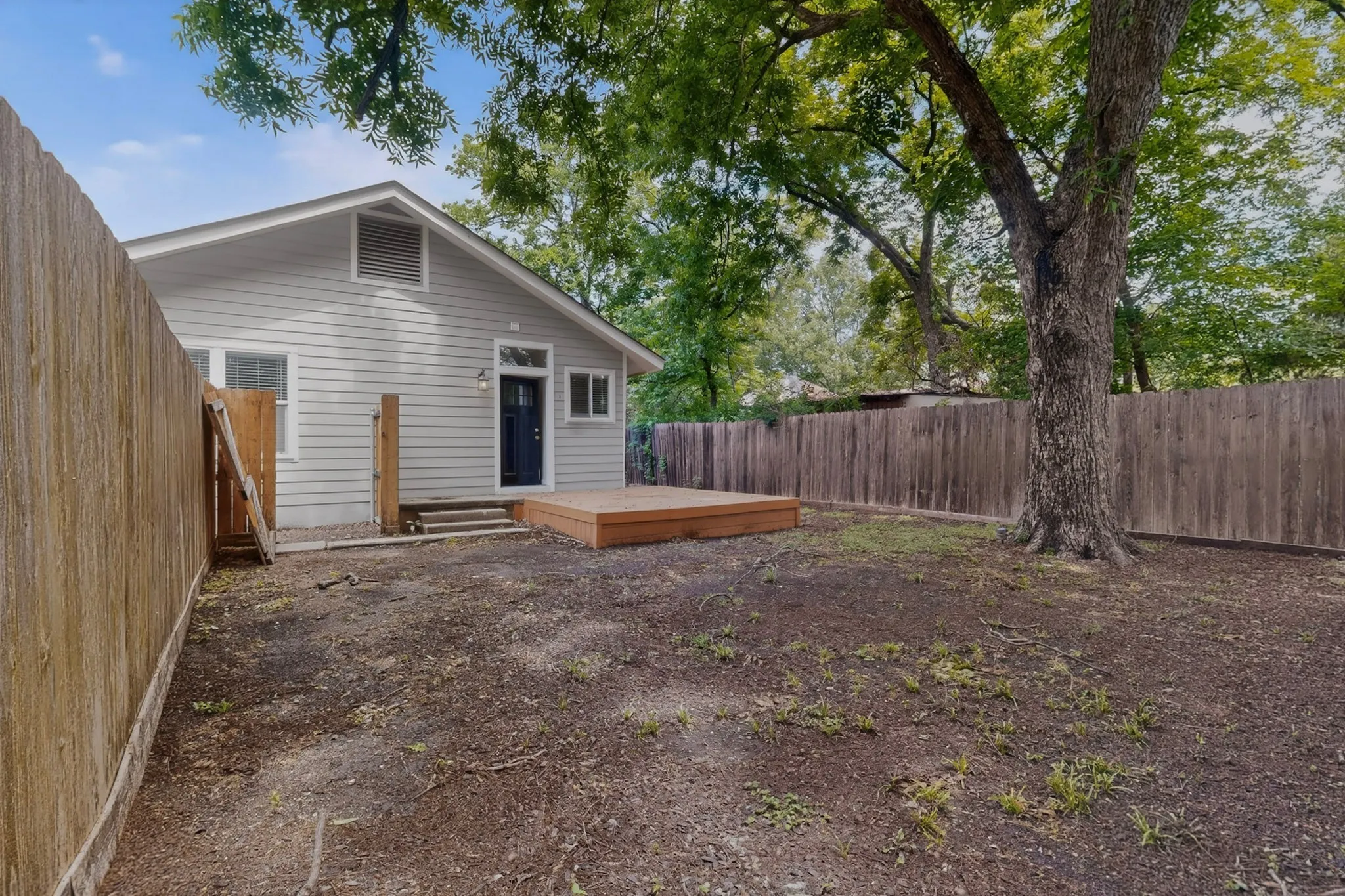 Rear exterior with wood decking, light gray siding, and a dark entry door