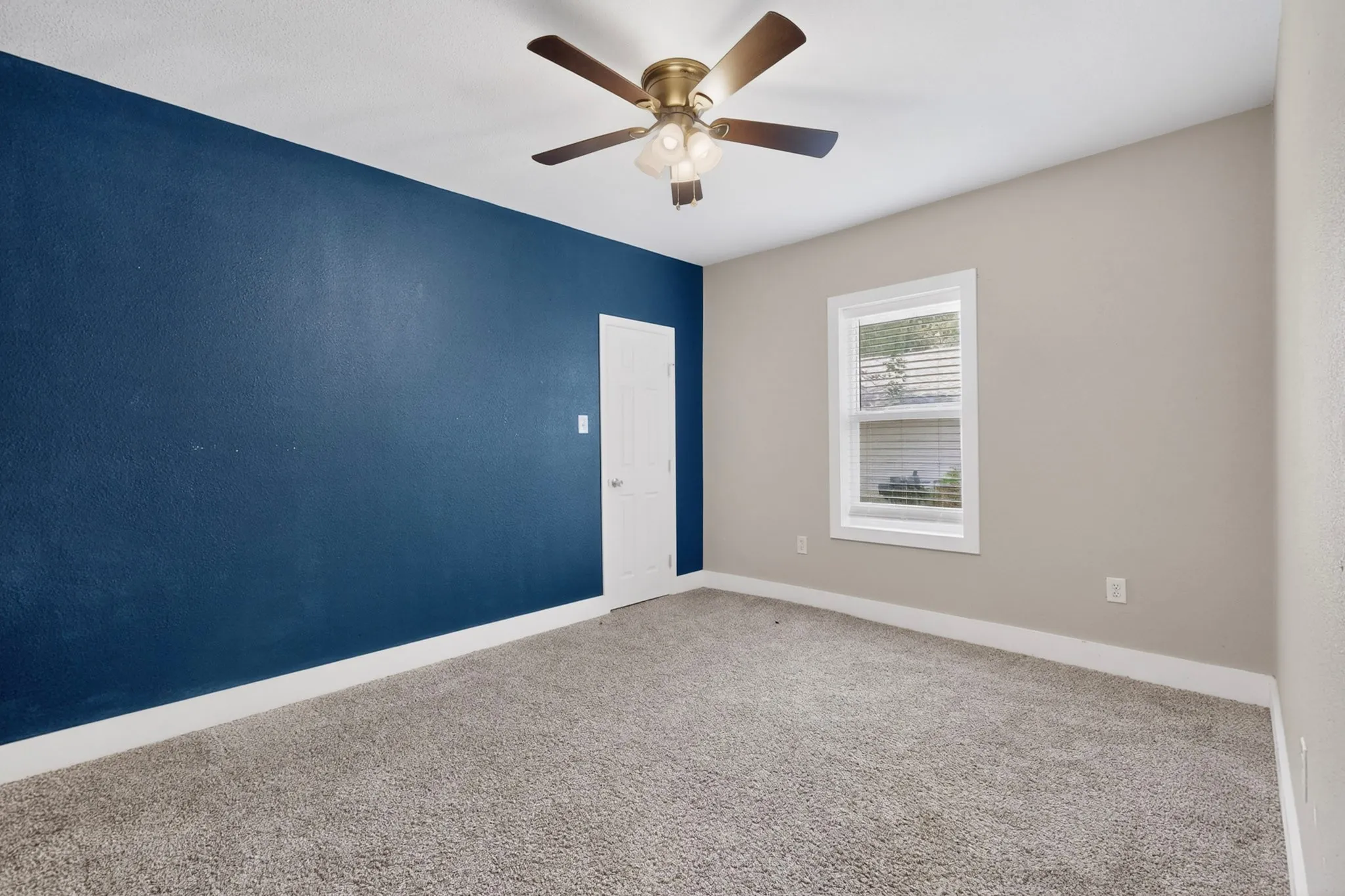 Carpeted interior room featuring a contrasting accent wall, a white painted door, and a single window with blinds