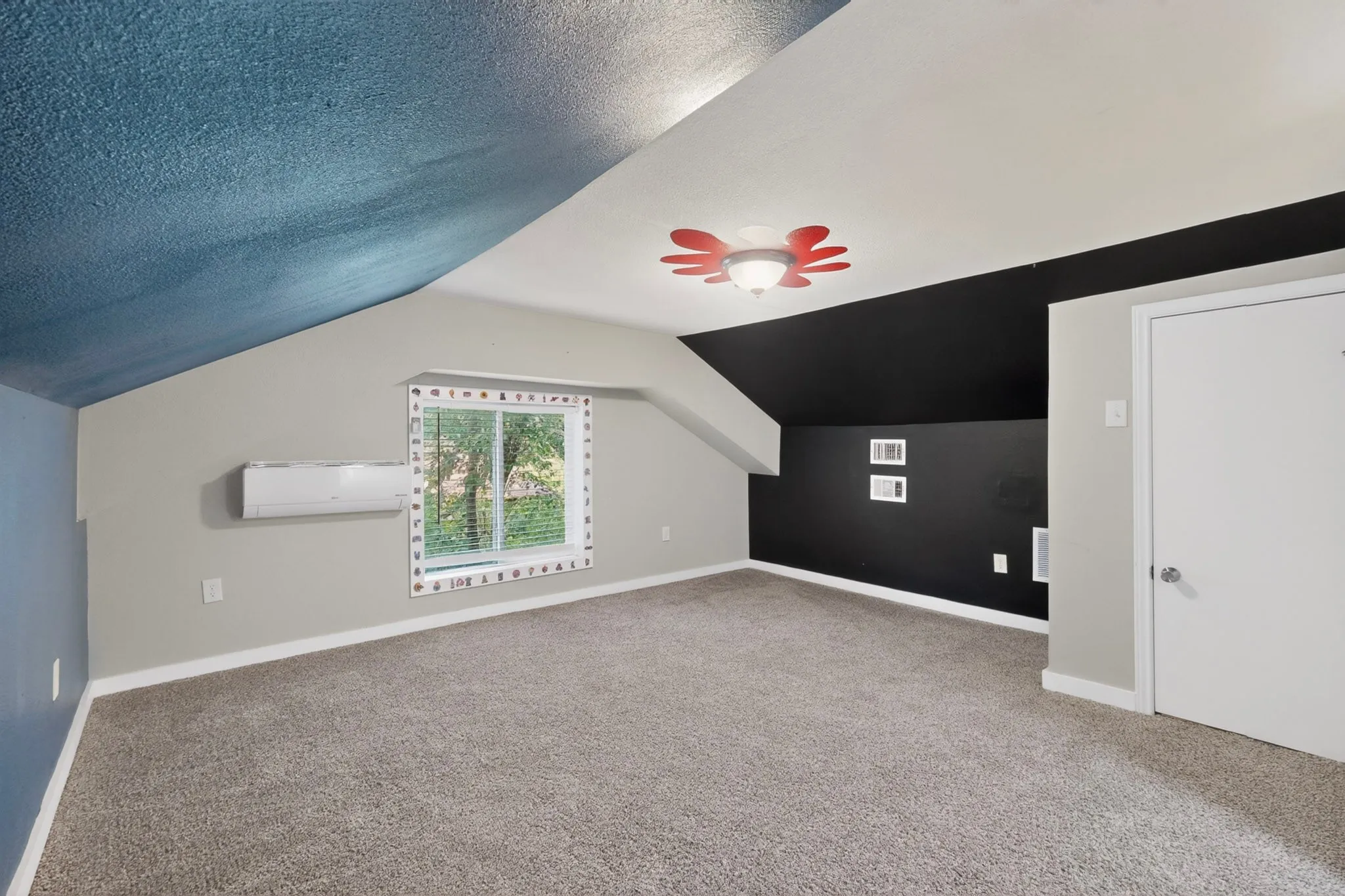 Spacious room featuring sloped ceilings, plush gray carpeting, and a window with horizontal blinds