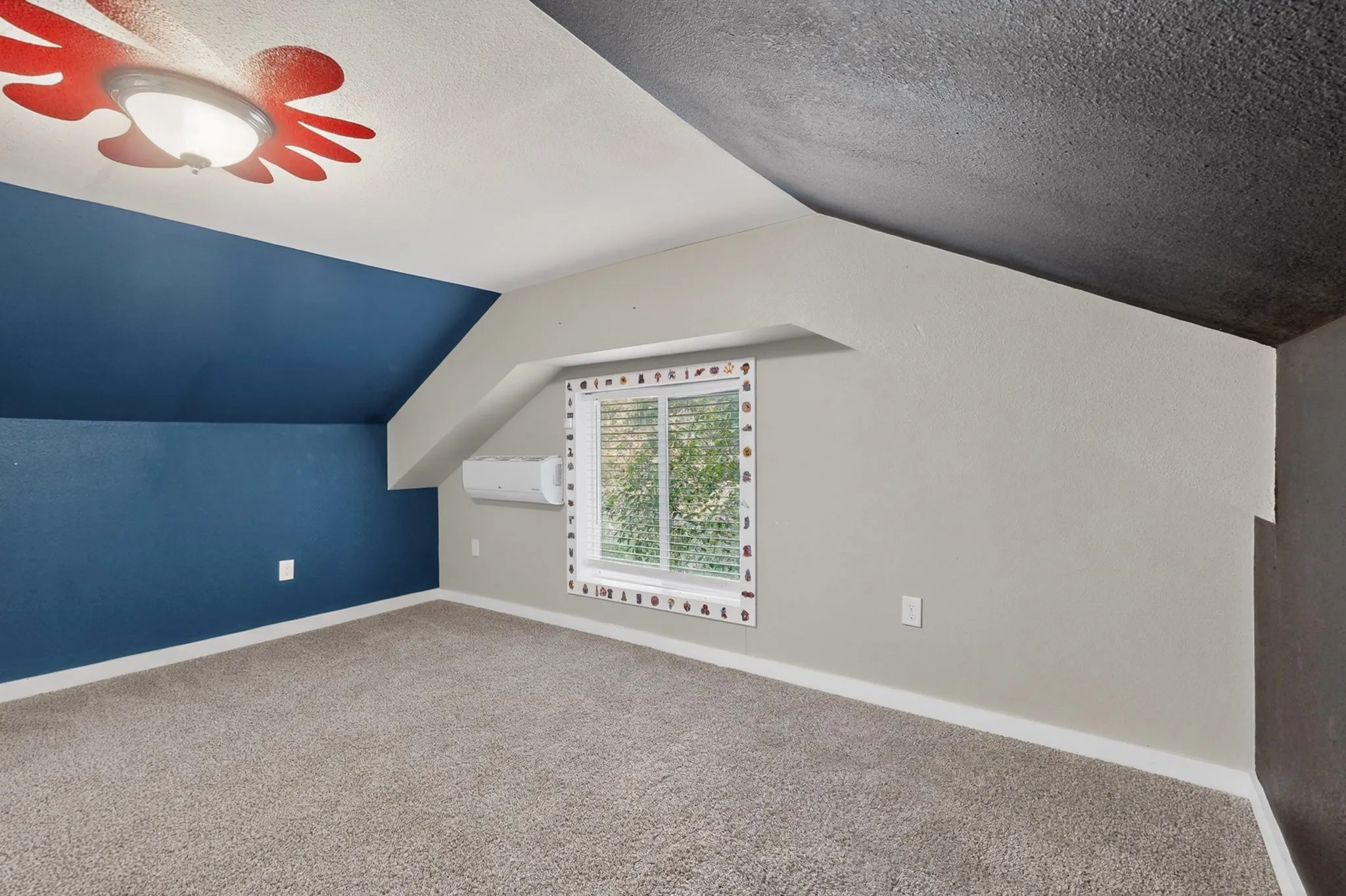 Carpeted room featuring a window with blinds, a wall-mounted AC unit, baseboards, and a ceiling light fixture