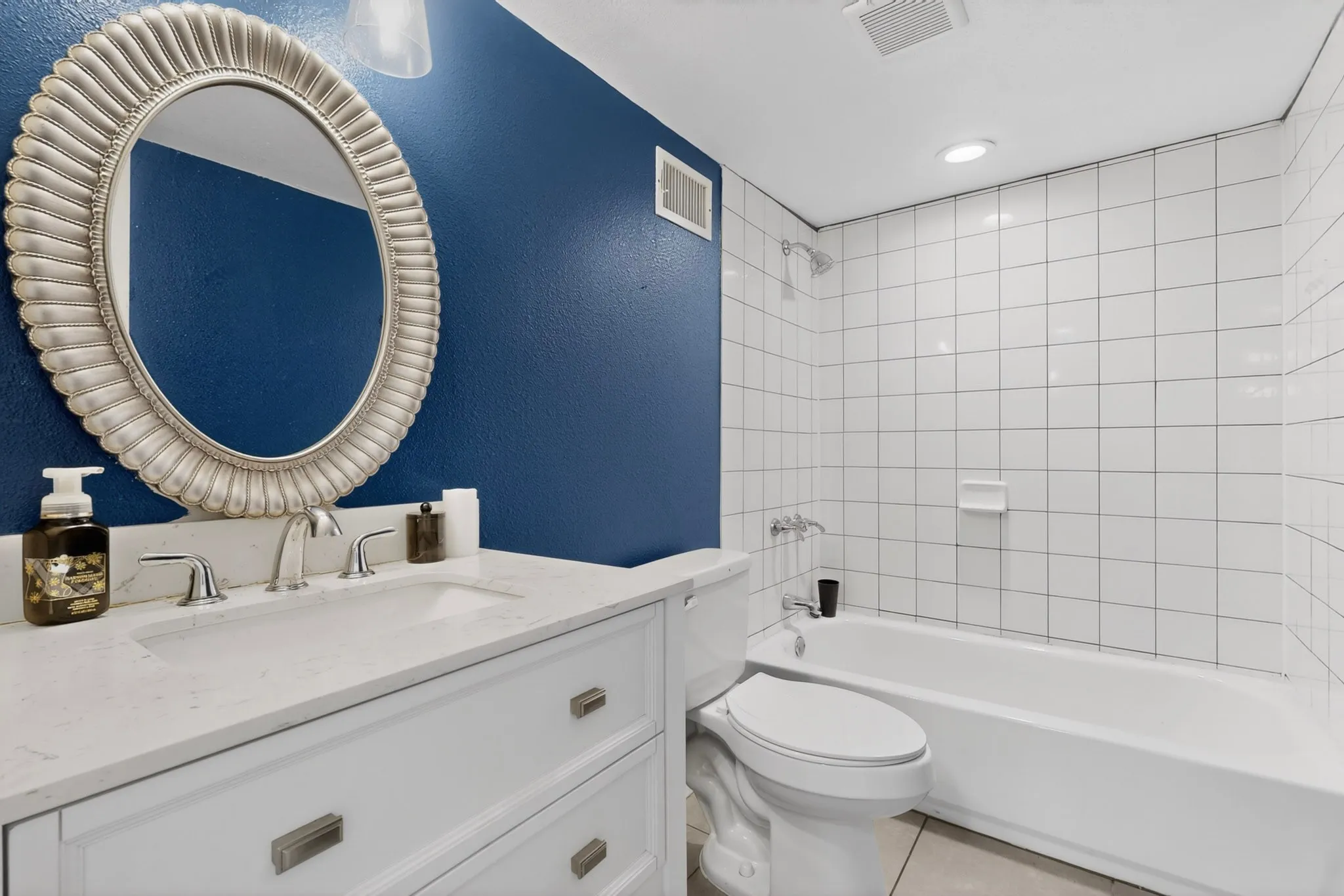 Bathroom featuring a white vanity with a light-colored countertop, an oval mirror with a decorative frame, and a bathtub with white subway tile surround