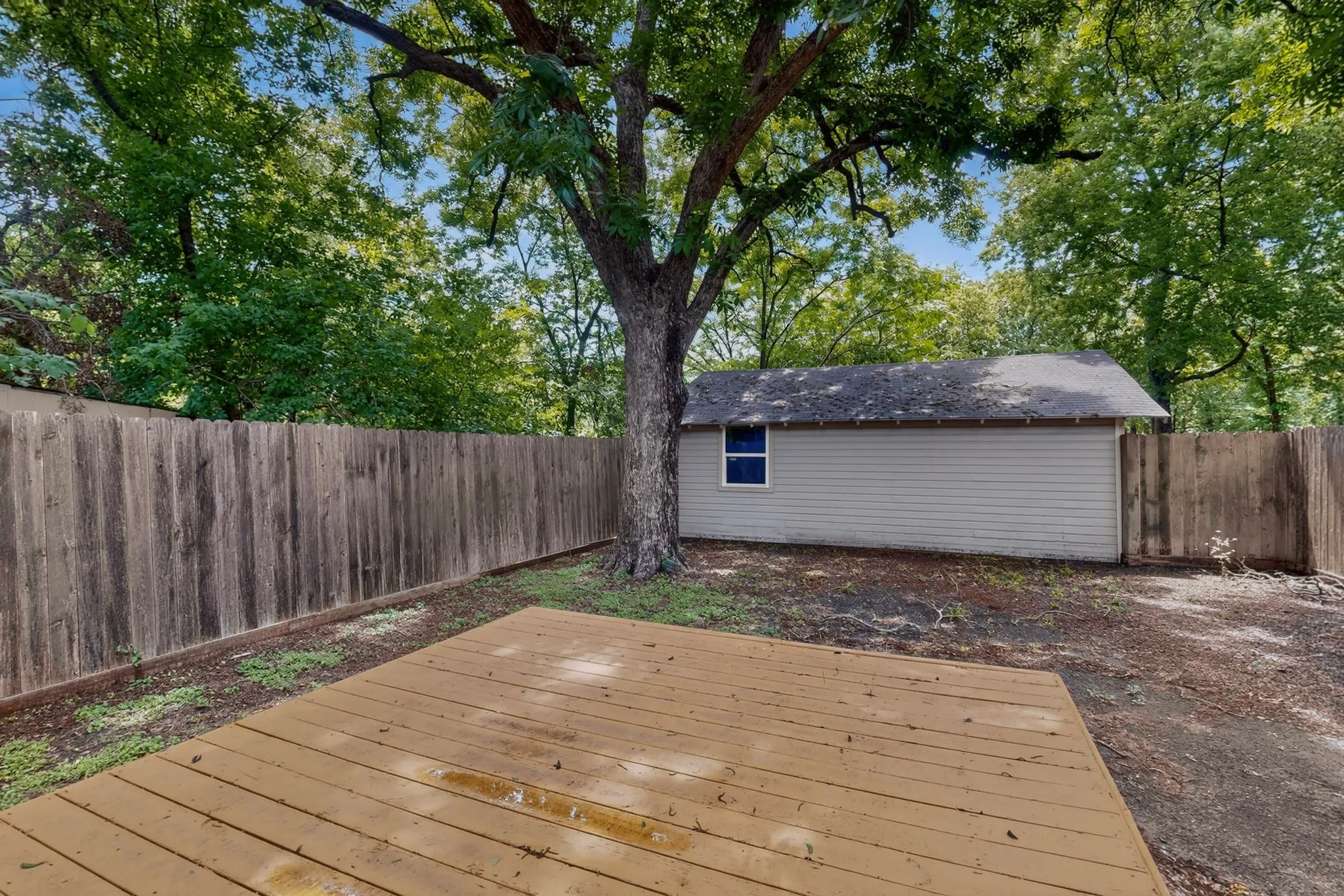 Outdoor decking area featuring wood-finish planks, surrounded by a wood privacy fence and mature trees