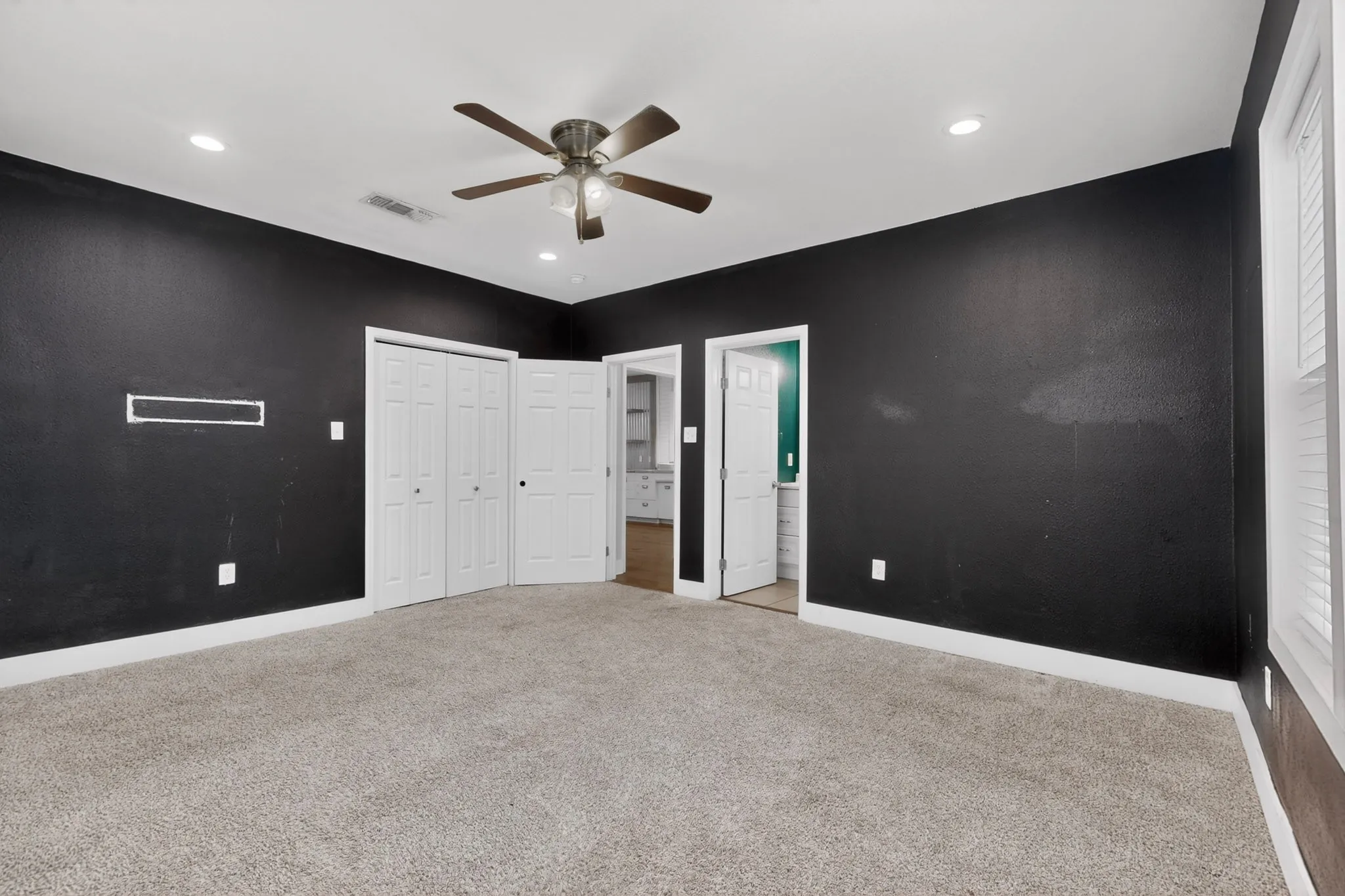 Spacious room featuring dark-painted walls, light-toned carpeting, and white baseboards