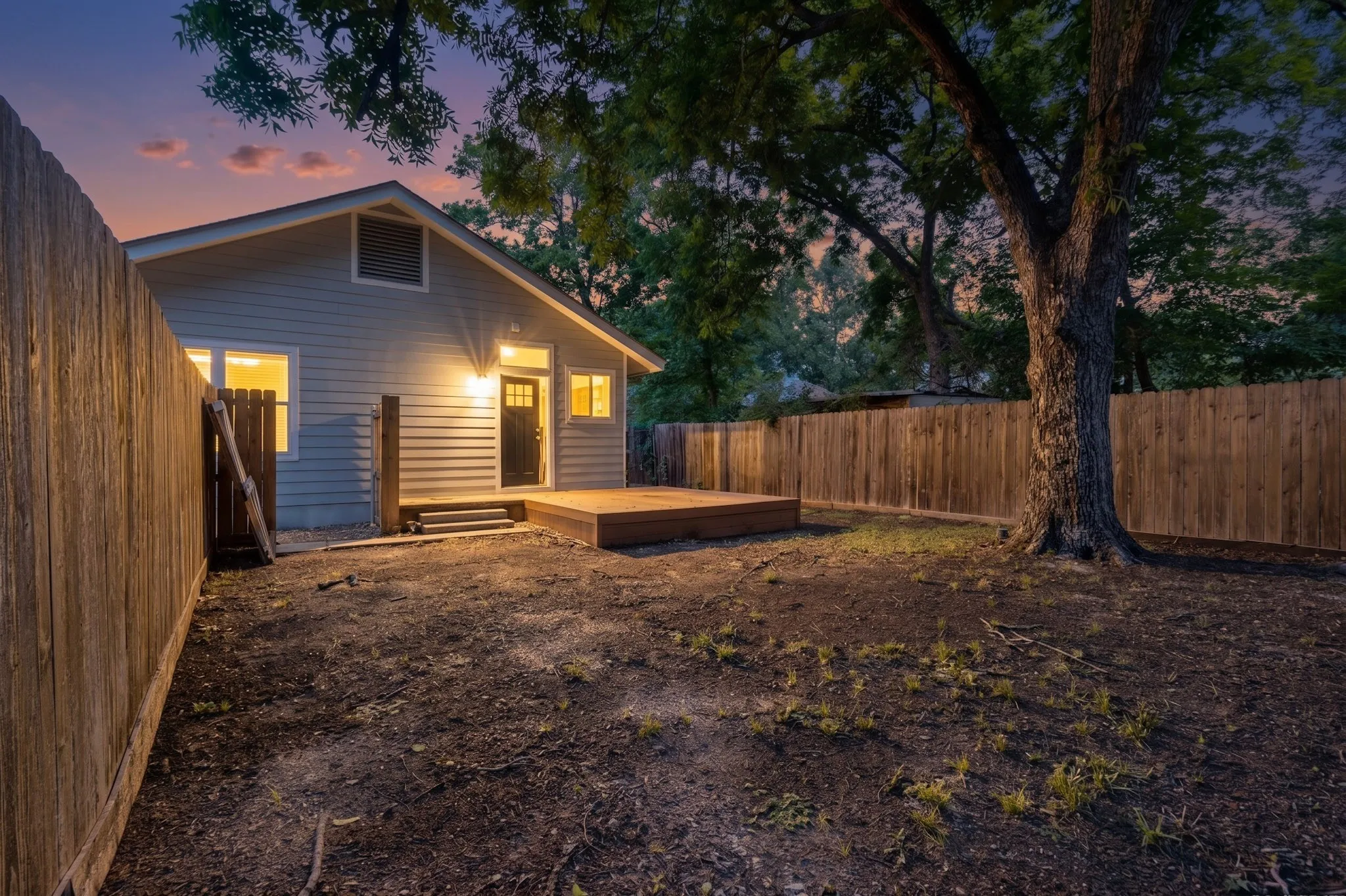 Private backyard featuring a wooden privacy fence, a newly installed wooden deck, exterior lighting, and mature trees