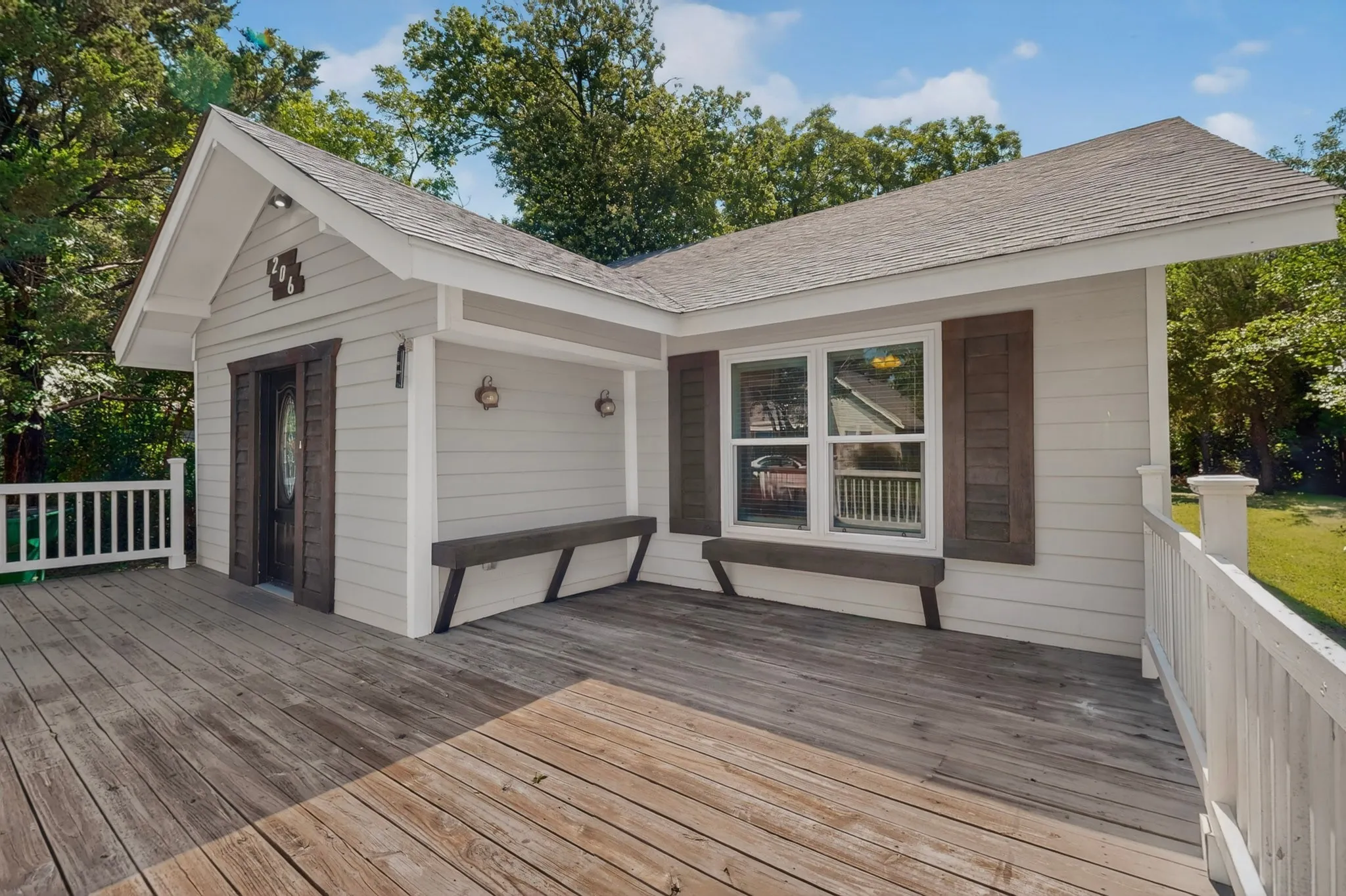 Expansive wooden deck with white railings extending from a structure featuring light siding and a gabled roof