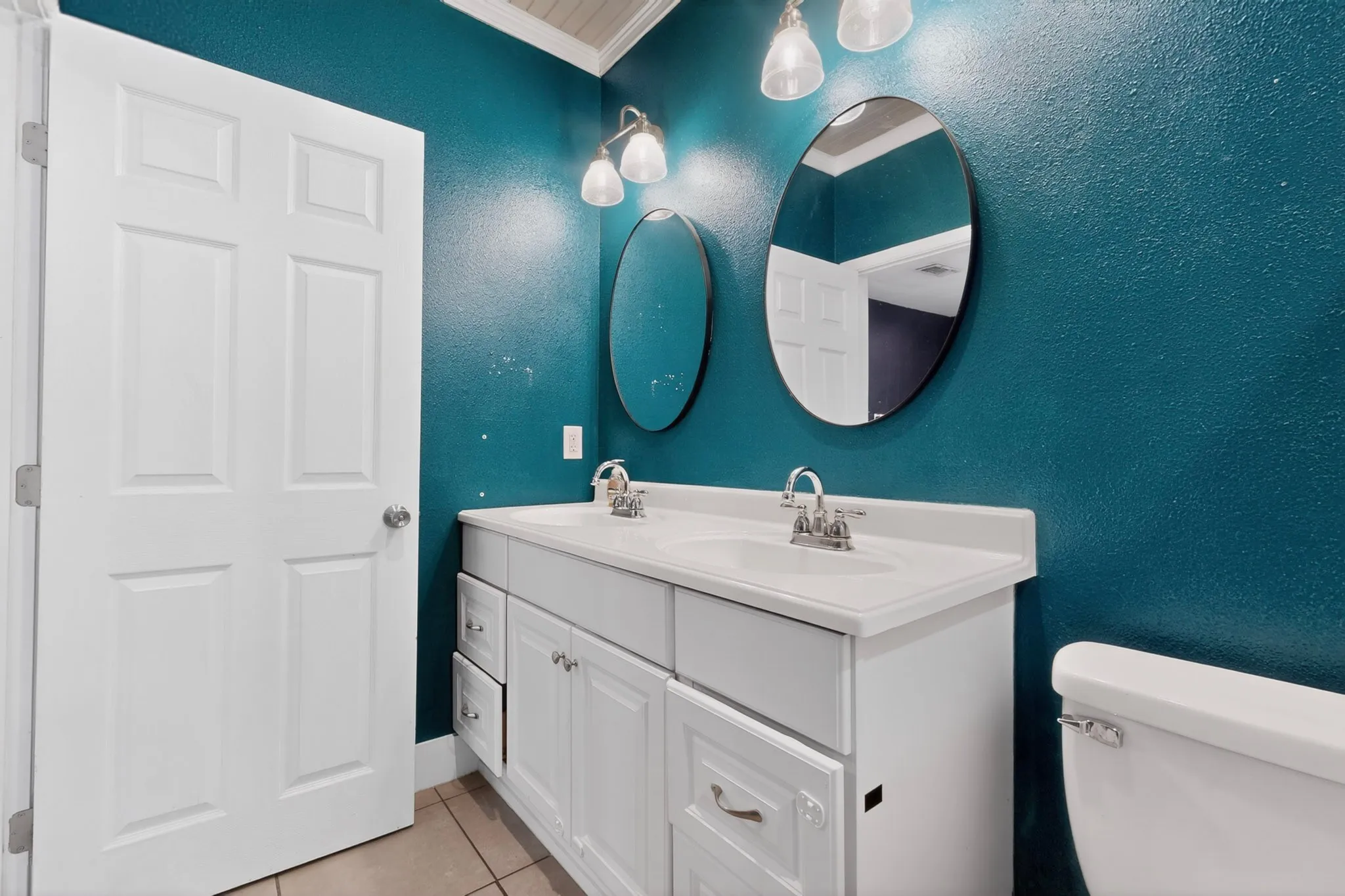 Dual vanity featuring white cabinetry, integrated sinks, chrome faucets, and oval mirrors