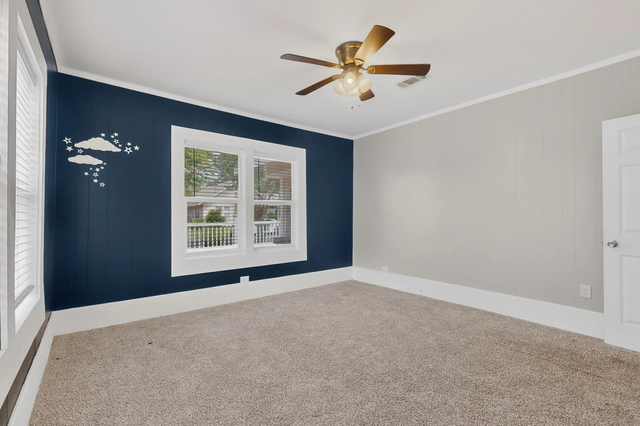 Carpeted room with a ceiling fan, white trim, and a paneled accent wall in a deep blue hue