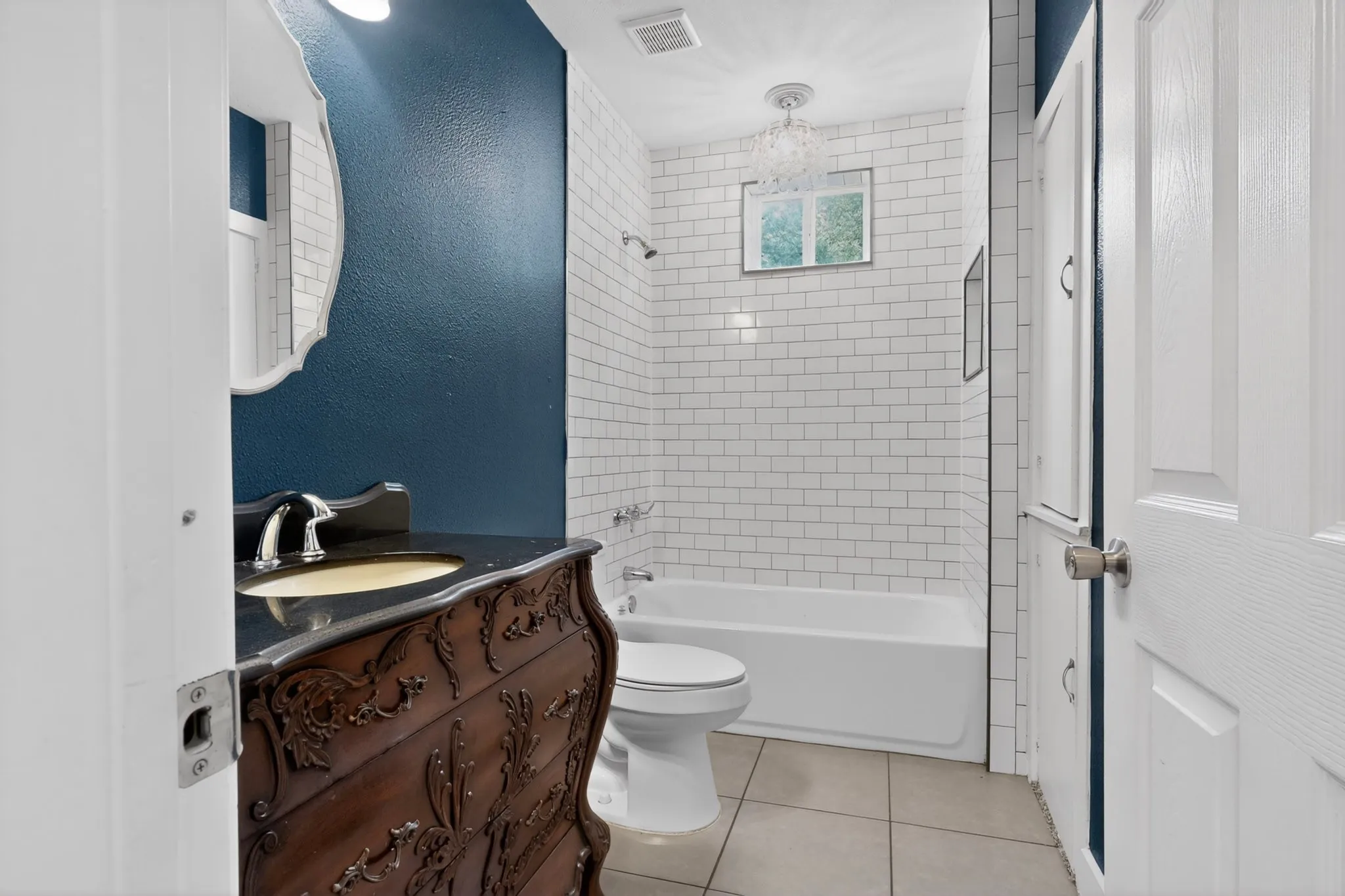Bathroom featuring a carved wood vanity with a dark countertop and undermount sink, white subway tile shower surround, window with natural light, and a decorative ceiling fixture