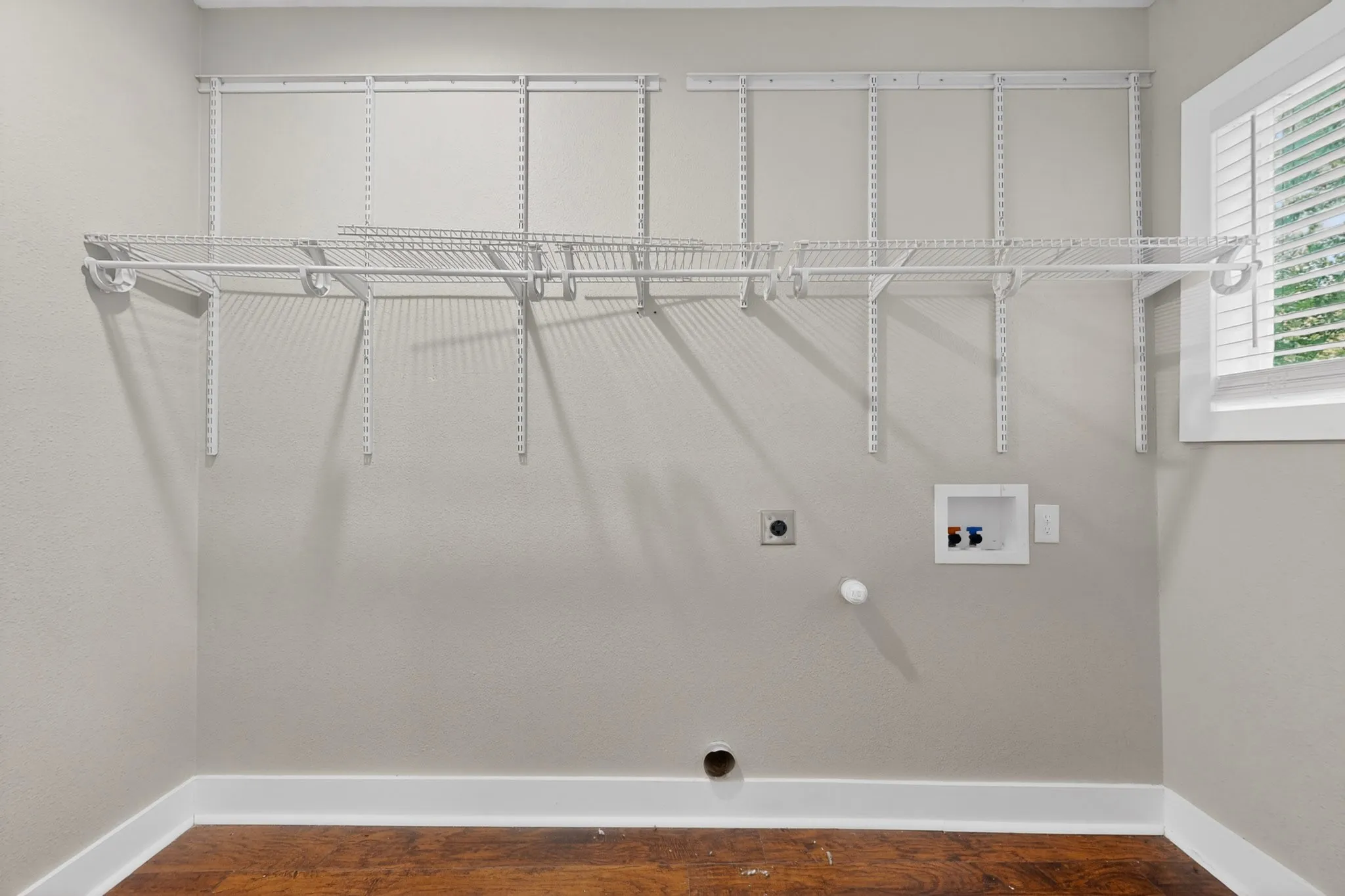 Laundry room featuring wood-finish flooring, white baseboards, a utility sink hookup, and a window with blinds