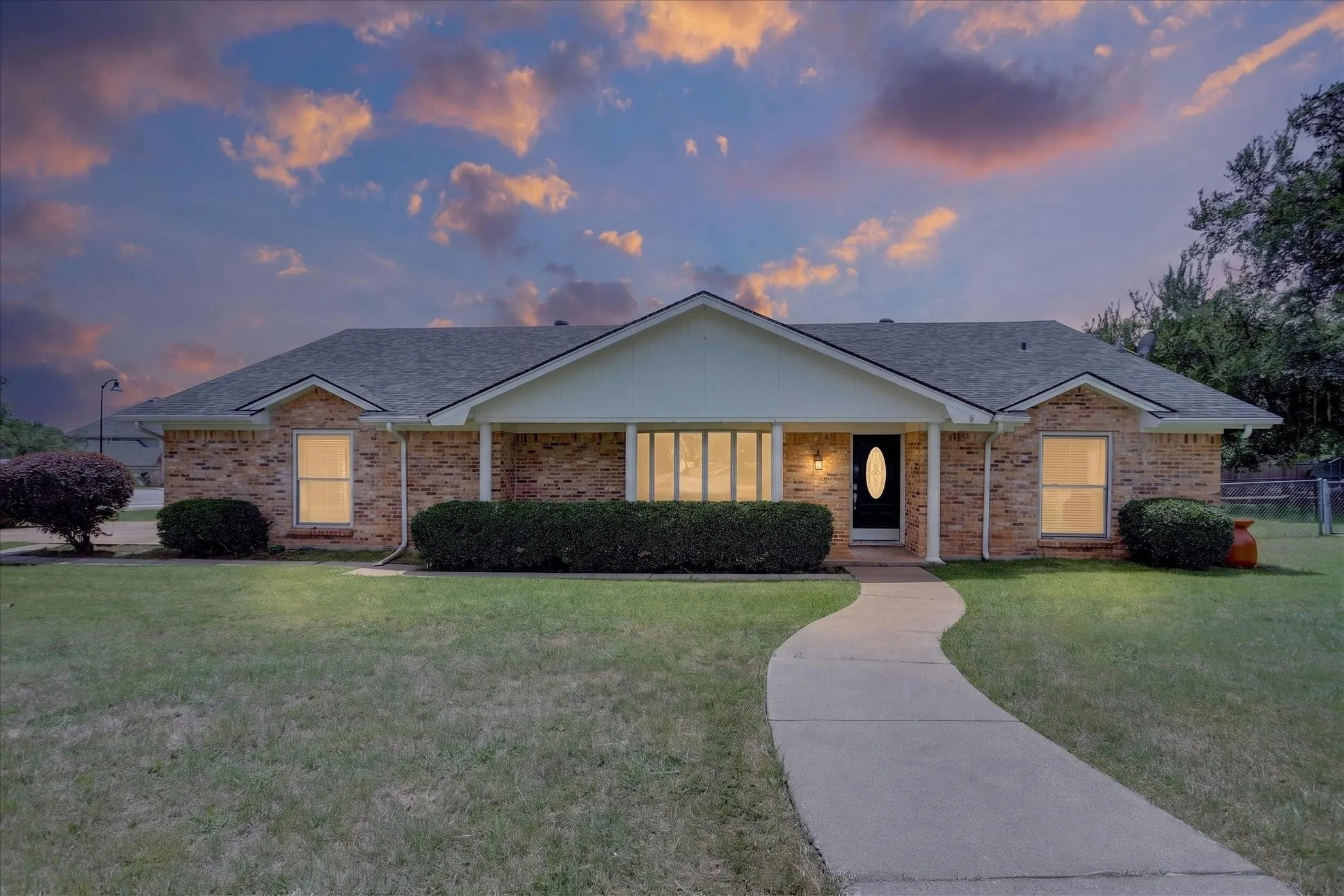 Traditional brick exterior featuring a covered front porch, an arched entry door, and a curved concrete pathway virtual twilight