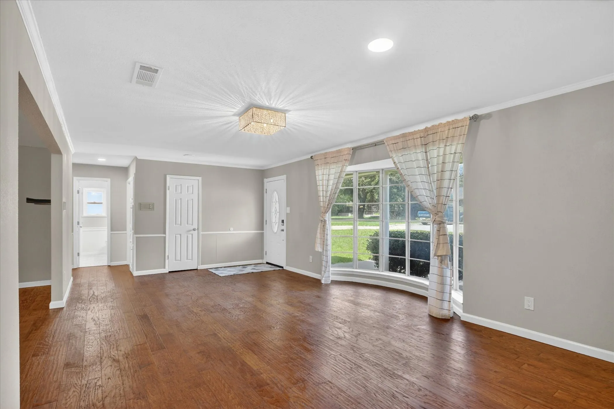 Spacious front room featuring wood-finish flooring, a decorative oval glass door, and a curved window with multiple panes