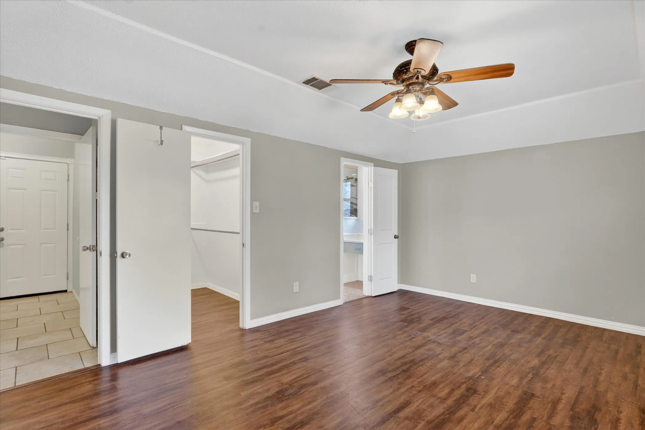Spacious room featuring wood-finish flooring, a tray ceiling, and a ceiling fan with integrated lighting