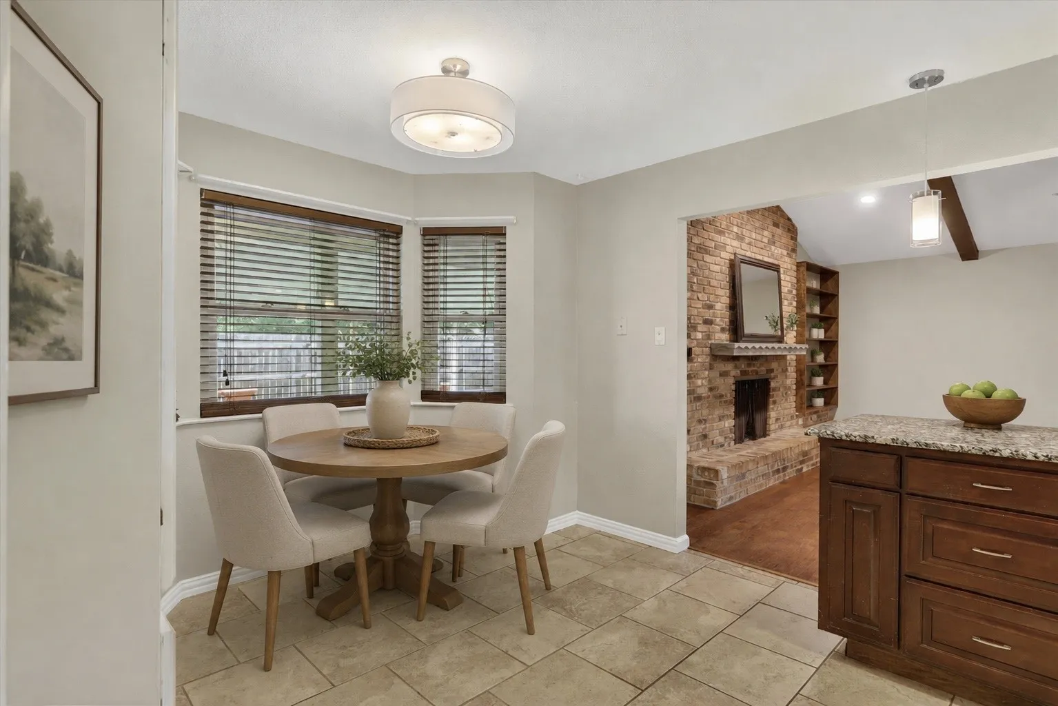 Virtually Staged. Light-colored tile flooring, breakfast nook with bay windows, wood-finish blinds, built-in cabinetry with stone countertop, exposed brick fireplace with wood mantel