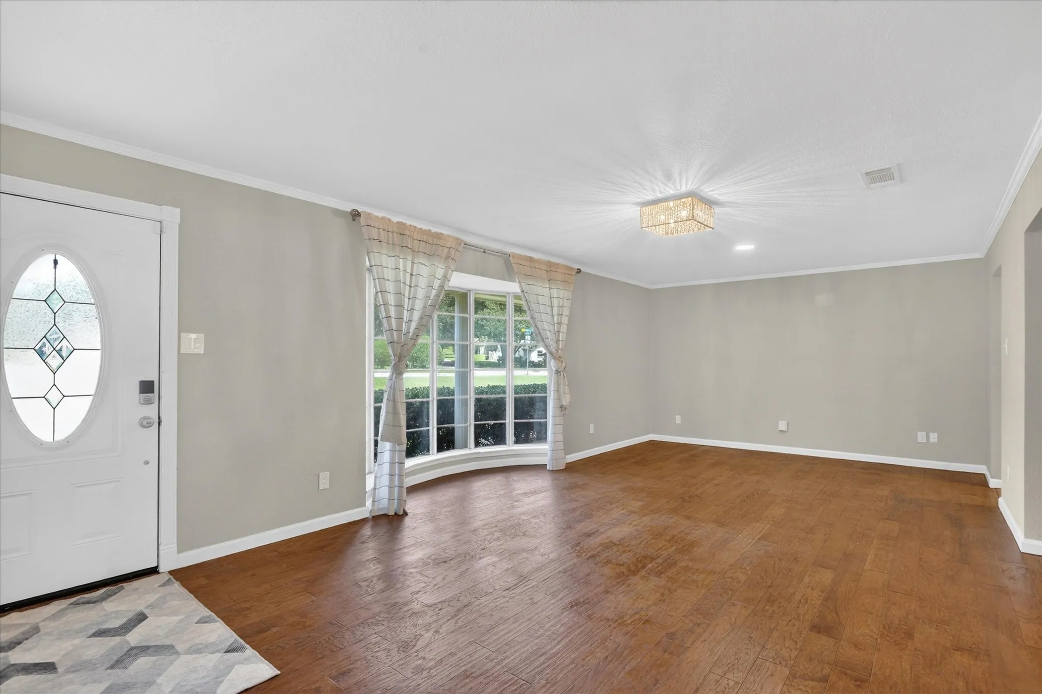 Spacious front room featuring wood-finish flooring, a decorative oval glass door, and a curved window with multiple panes