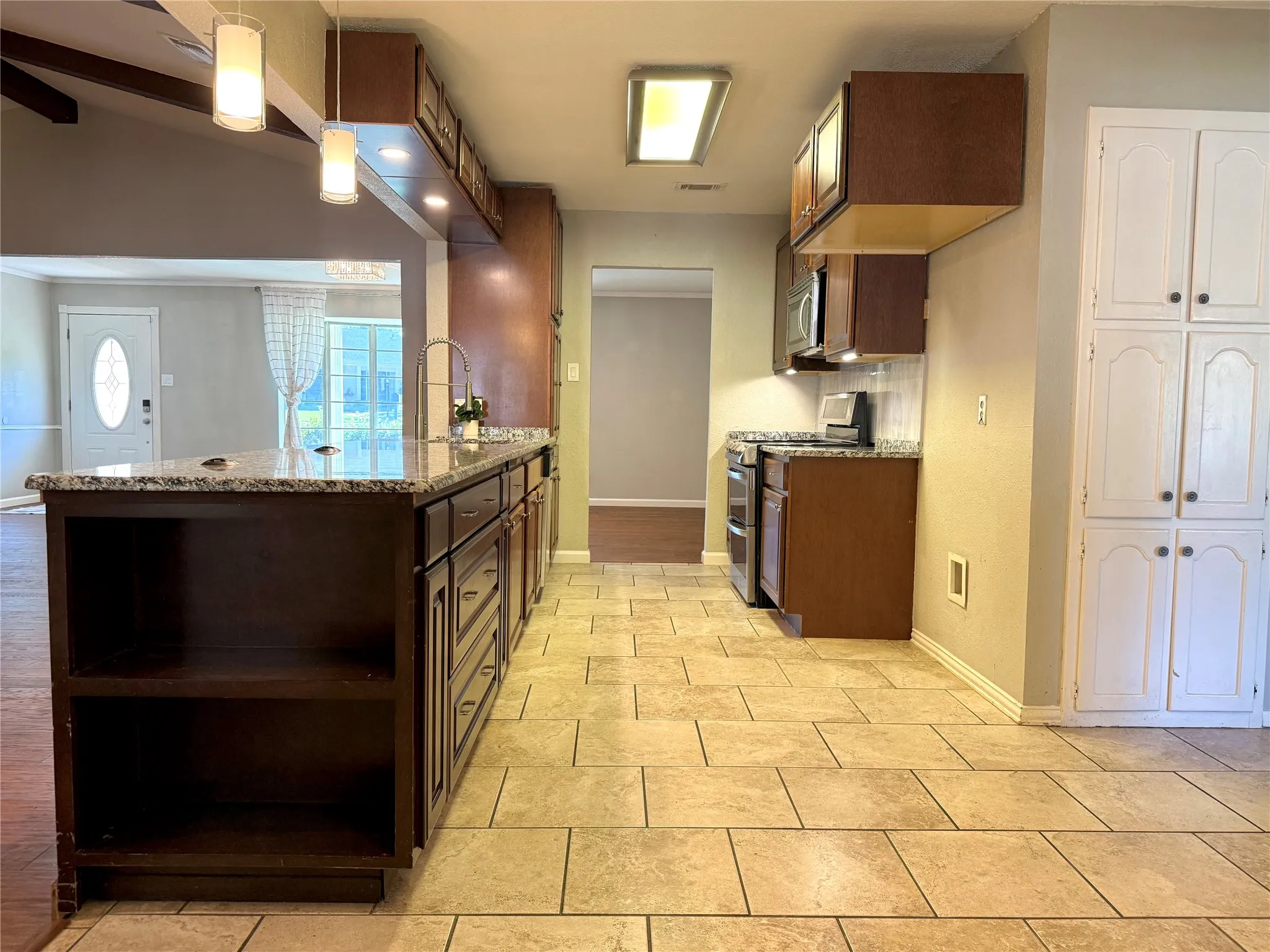 Kitchen featuring an expansive island with a granite countertop, dark wood-finish cabinetry, and contemporary pendant lighting