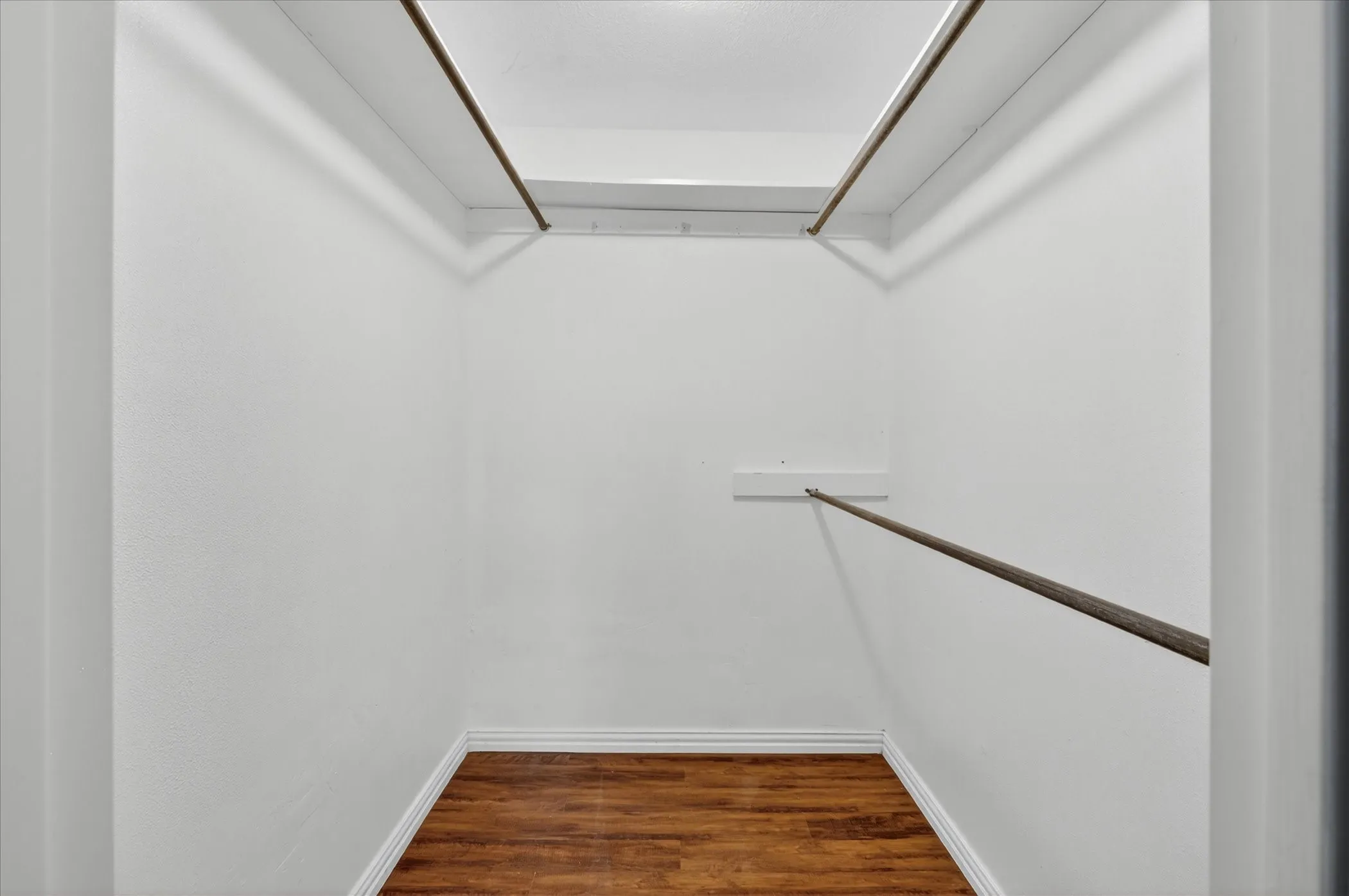 Walk-in closet featuring white walls, wood-finish flooring, white baseboards, and two levels of hanging rods