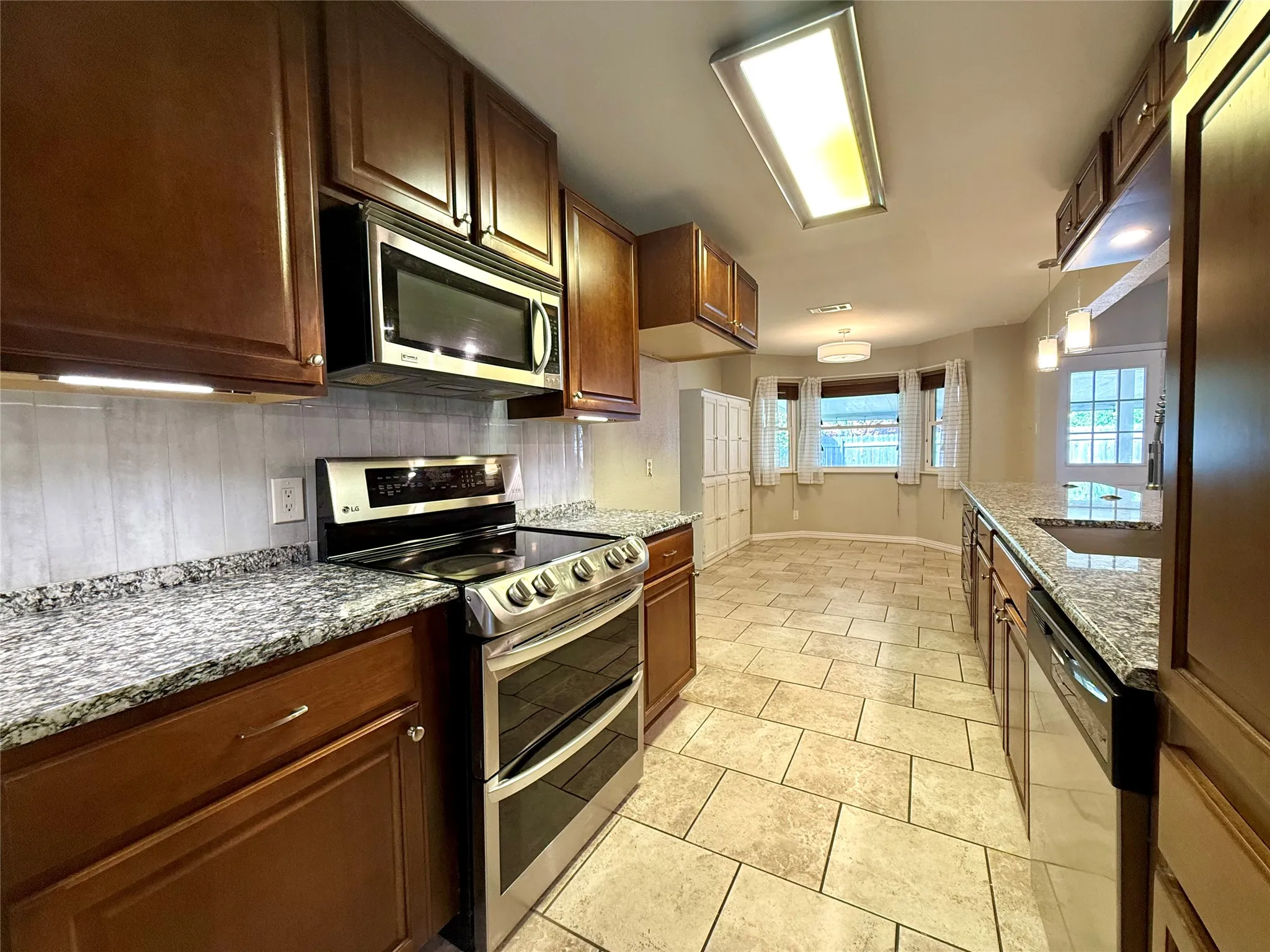 Kitchen featuring dark wood cabinetry, stainless steel appliances, a white tile backsplash, and granite countertops
