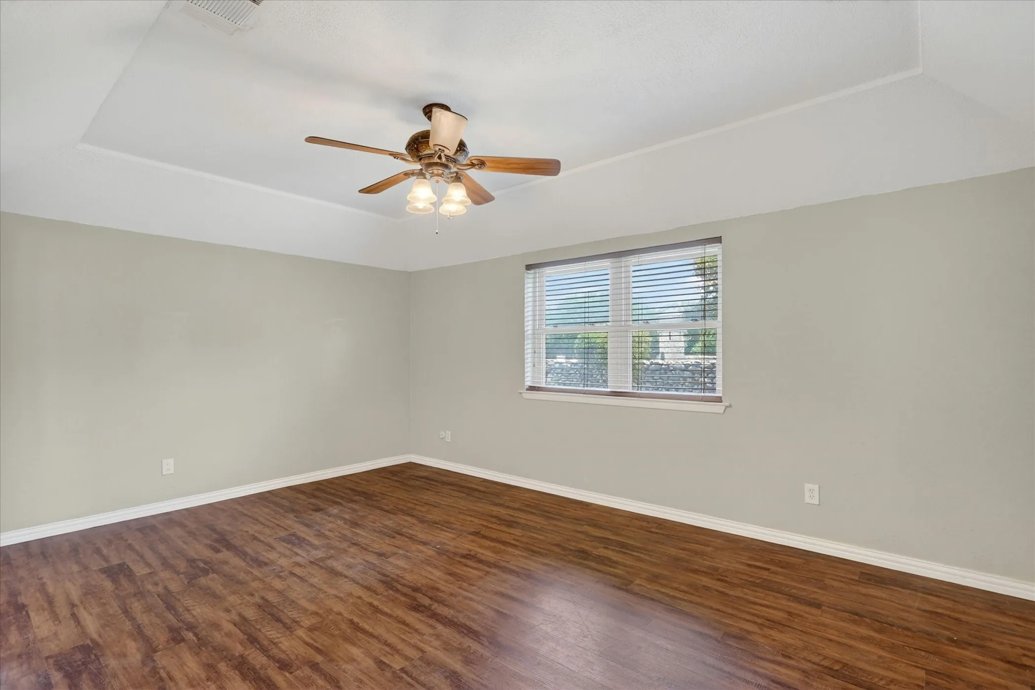 Tray ceiling with a ceiling fan light fixture, wood-finish flooring, and a large window with​​‌​​​​‌​​‌‌​‌‌​​​‌‌​‌​‌​‌​​​‌​​ blinds