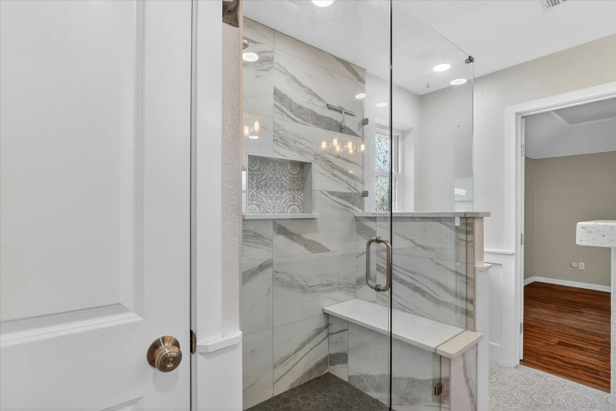 Glass-enclosed shower featuring large format tile walls, a built-in bench, and a decorative tile niche