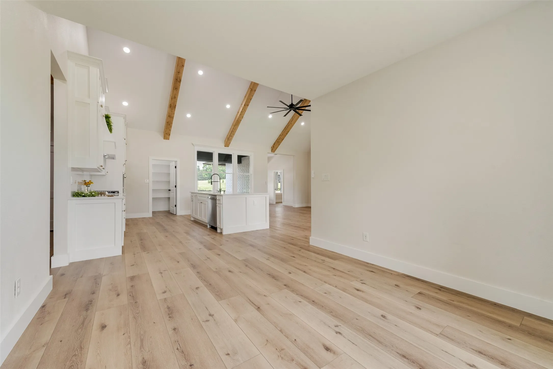 Spacious open-concept living area featuring light wood-finish flooring, vaulted ceilings with exposed wood beams, and recessed lighting