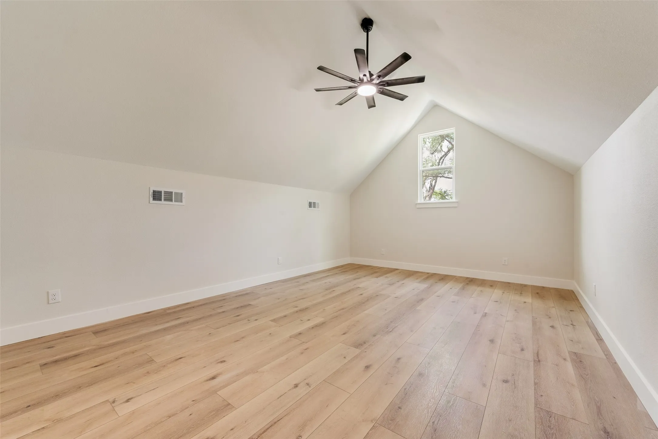 Spacious attic room featuring wood-finish flooring, a vaulted ceiling, and a modern ceiling fan with integrated lighting