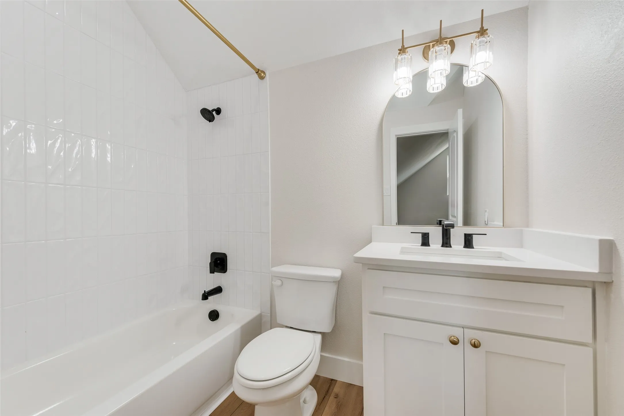Bathroom featuring a white bathtub with subway tile surround, matte black fixtures, and a brass shower rod