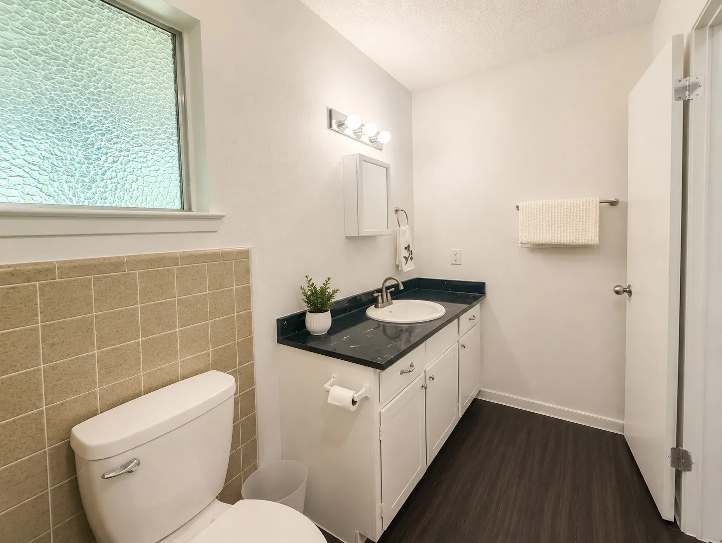 Bathroom featuring a single vanity with a dark countertop, white cabinetry, undermount sink, and wood-finish flooring