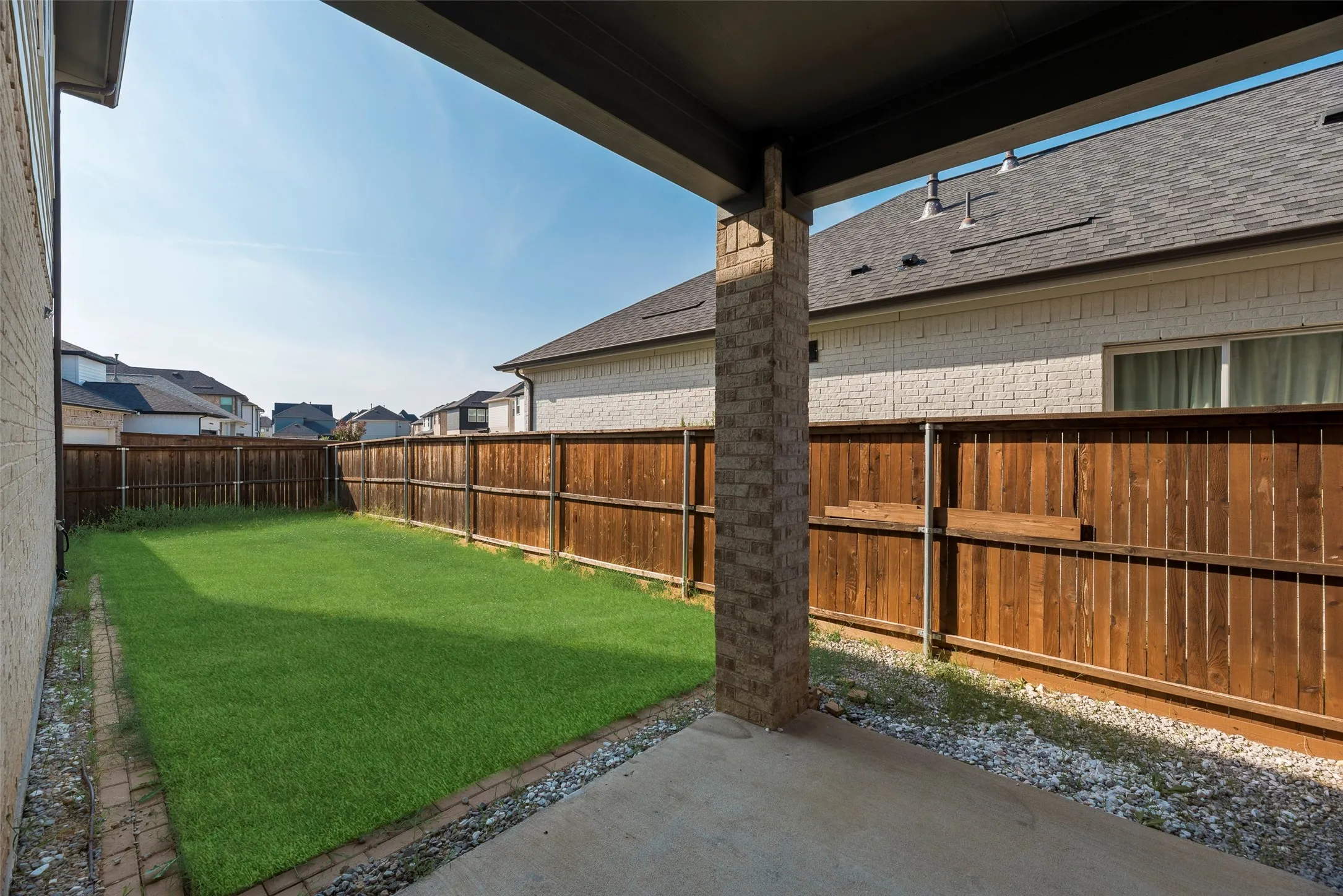 Covered concrete patio extending to a grass lawn, enclosed by wood privacy fencing