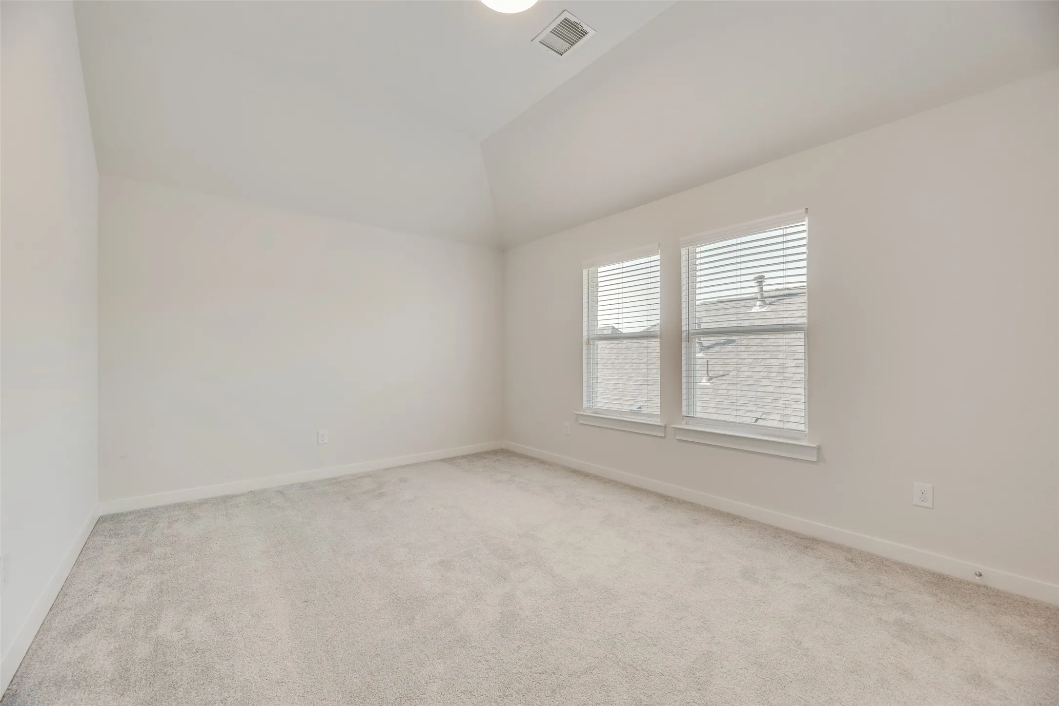 Carpeted room featuring a vaulted ceiling, recessed lighting, and two windows with blinds