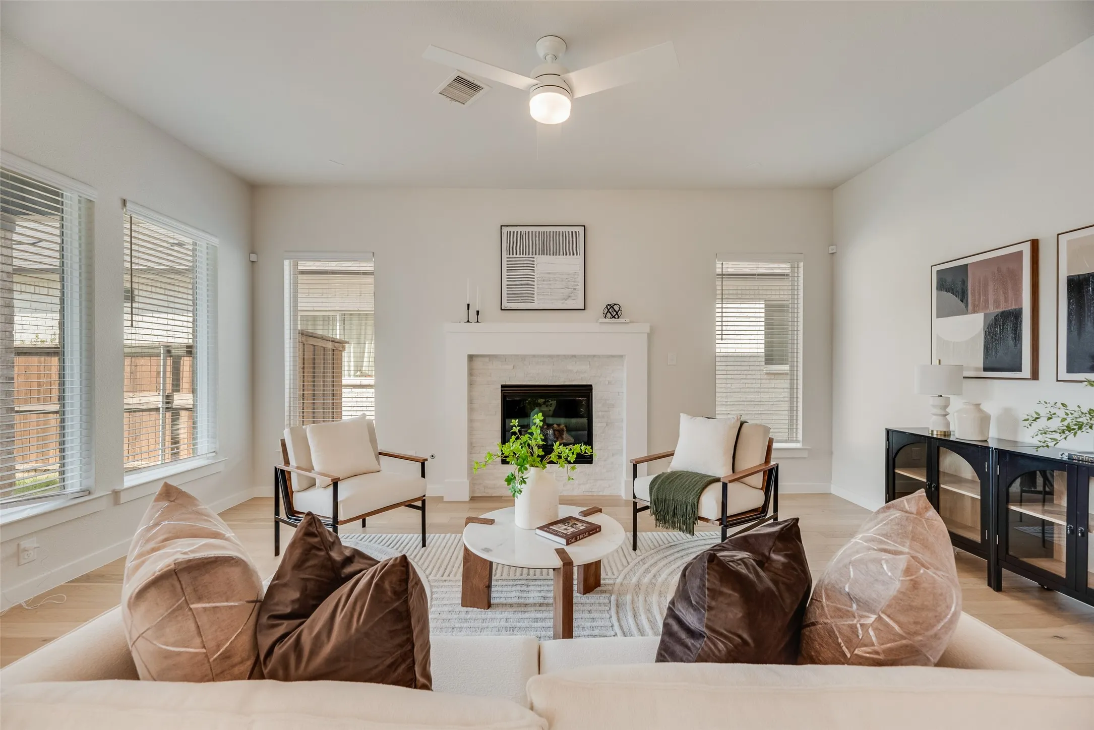 Spacious living area featuring light wood-finish flooring, a contemporary ceiling fan, and multiple windows with blinds