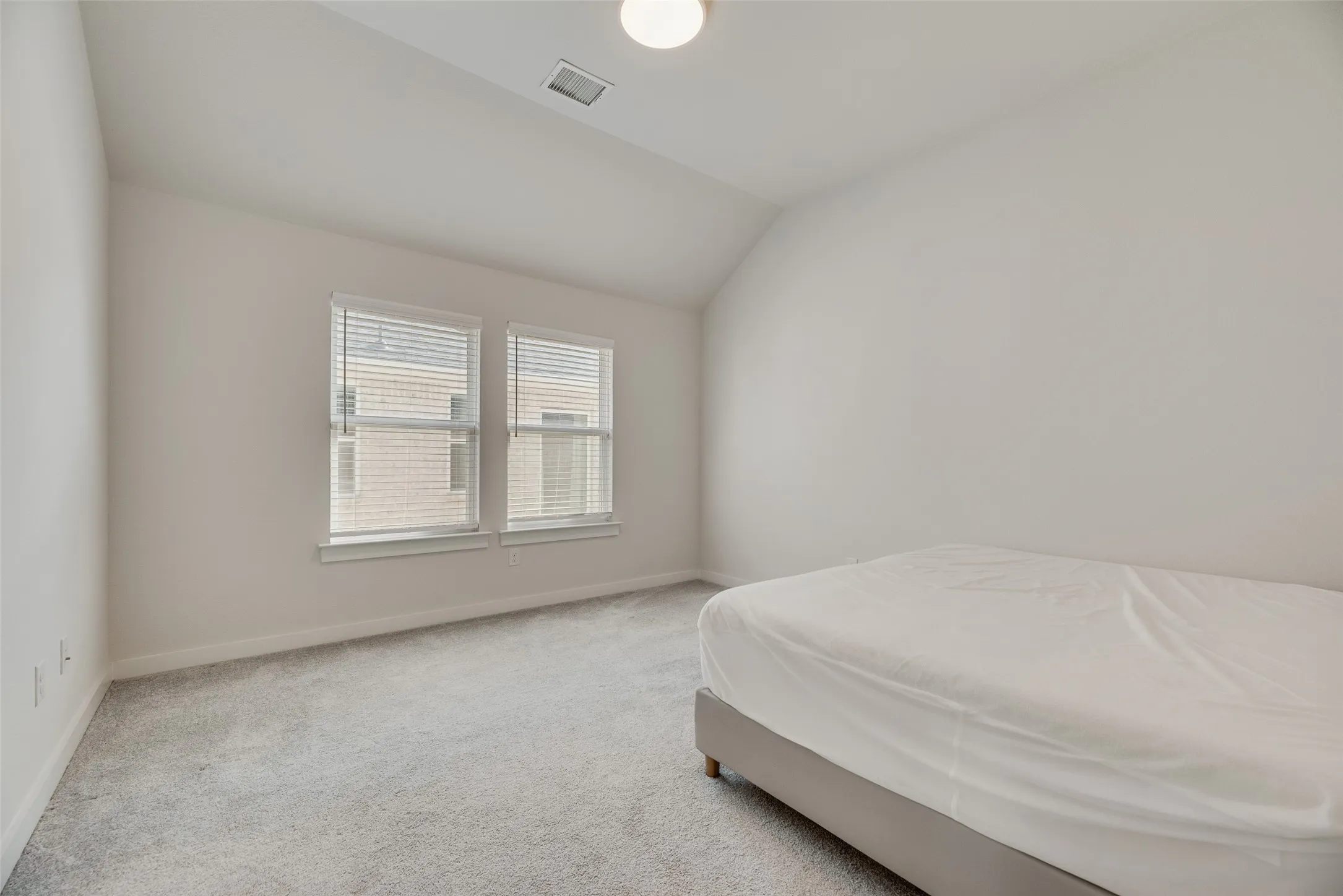 Carpeted room featuring a vaulted ceiling and dual windows with blinds