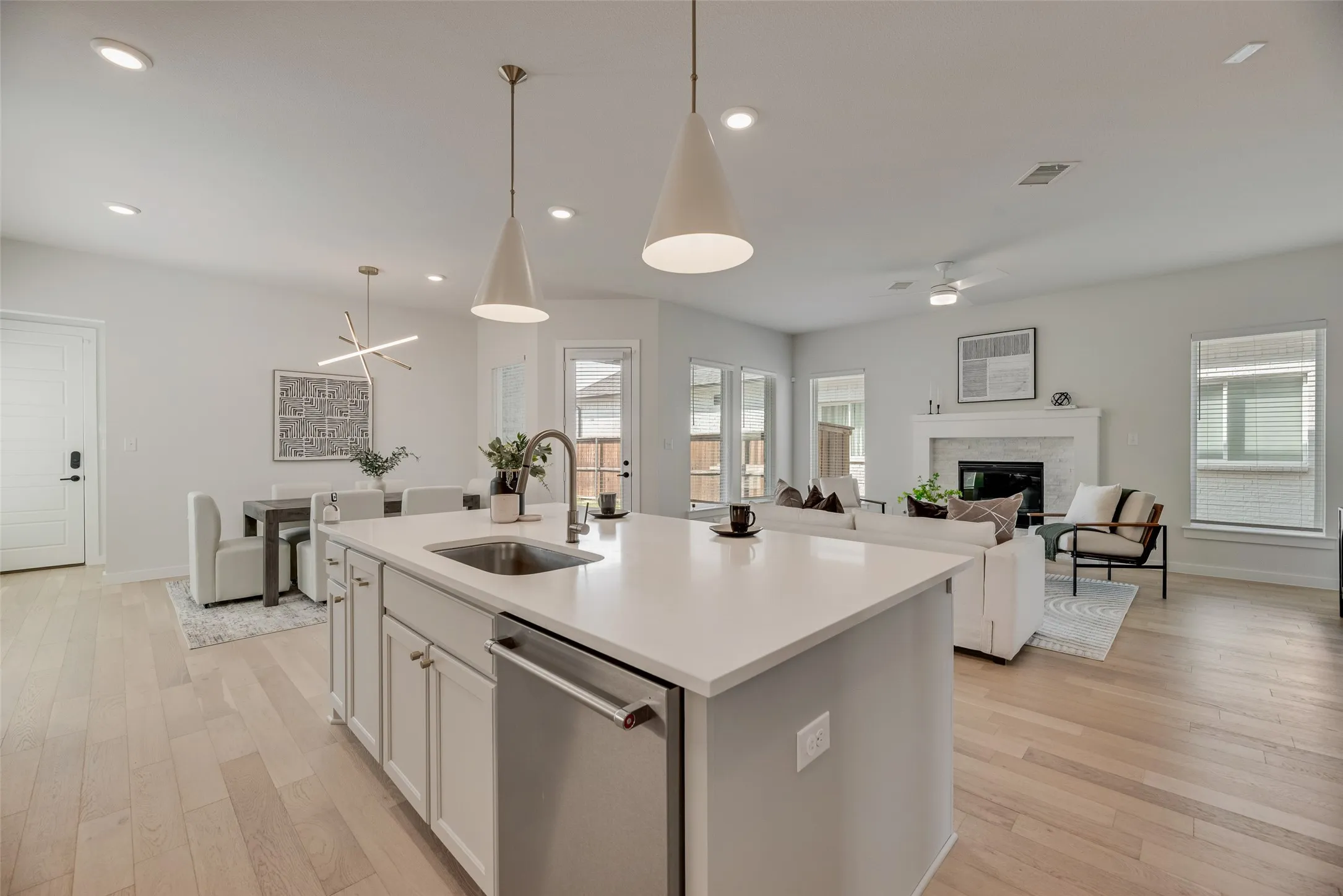 Open-concept living area featuring a kitchen island with sink, stainless steel dishwasher, and pendant lighting
