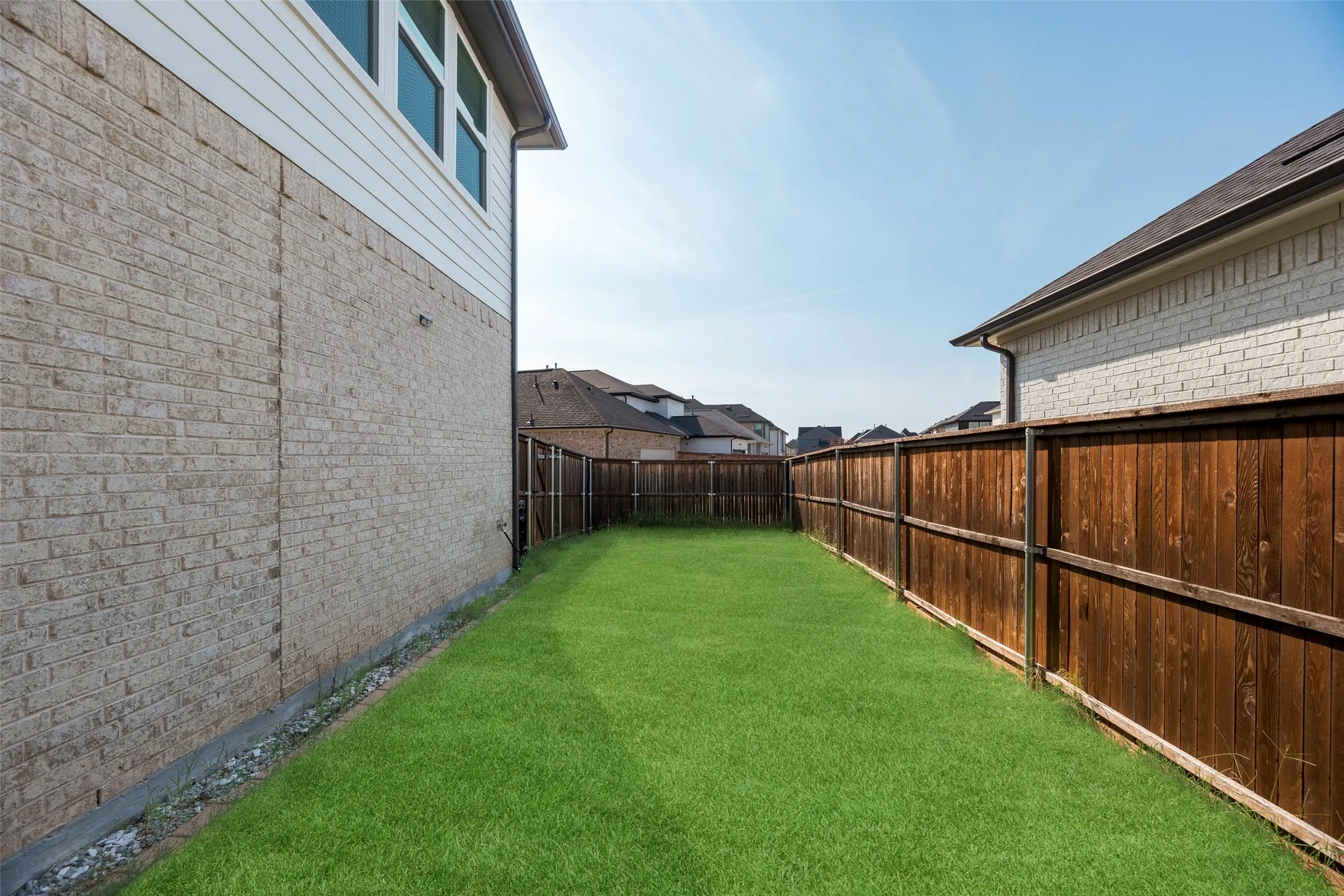 Private backyard featuring a well-maintained lawn, complete wood fencing, and a brick and siding exterior