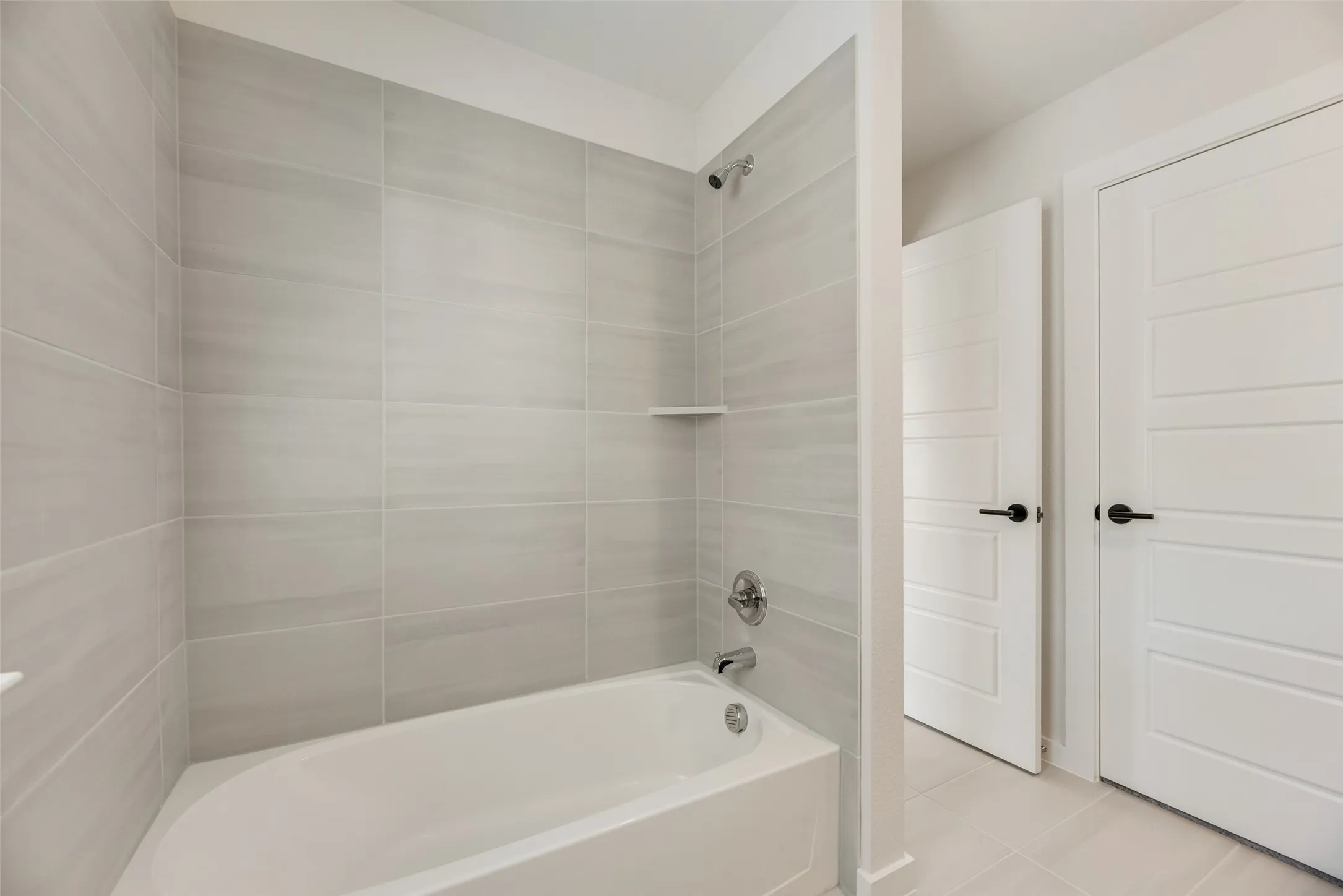 Bathroom featuring a white tub, chrome fixtures, and light gray rectangular wall tiles