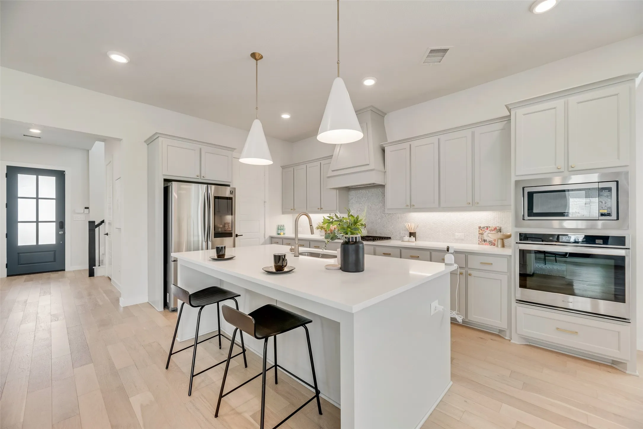 Open-concept kitchen featuring light wood-finish flooring, white cabinetry, a large kitchen island with pendant lighting, stainless steel appliances, and a built-in oven and microwave combination