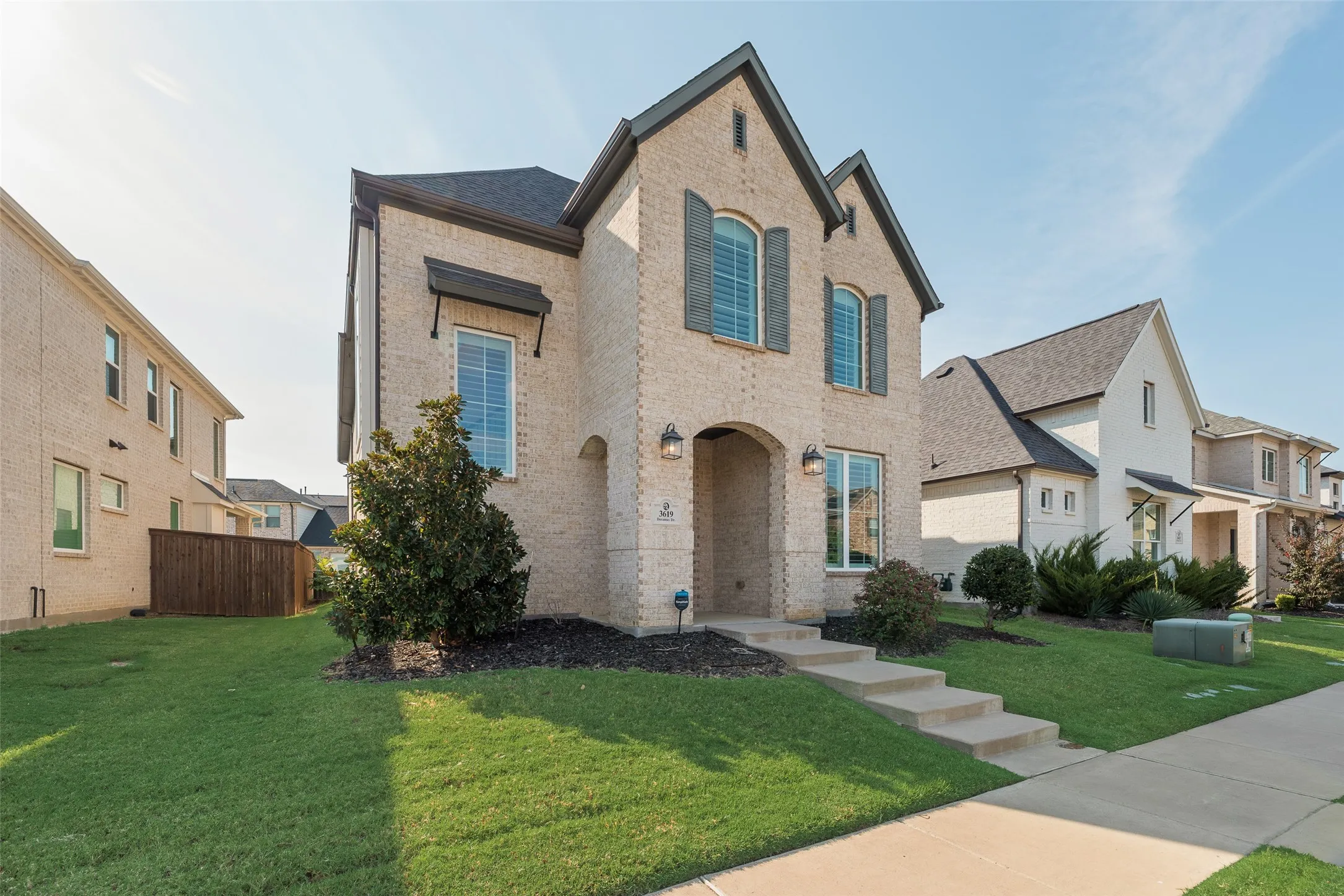 Brick exterior featuring arched entry, dark shutters, and a gabled roofline