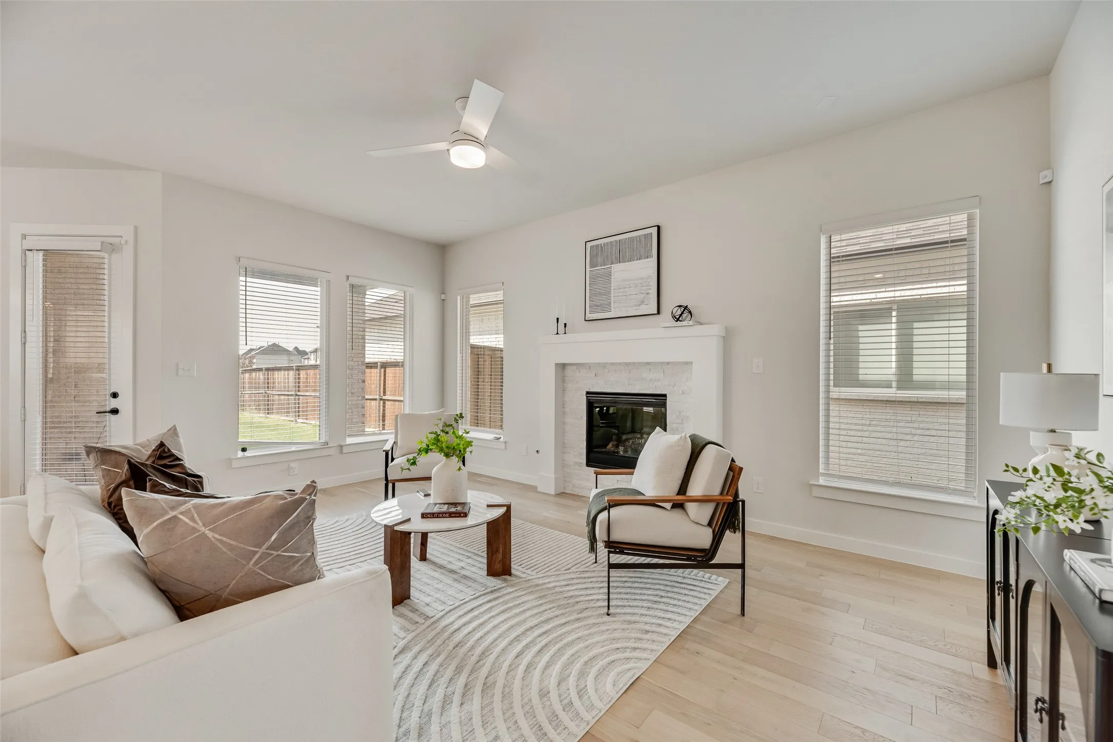 Bright living area featuring wood-finish flooring, a contemporary ceiling fan, and multiple windows with blinds