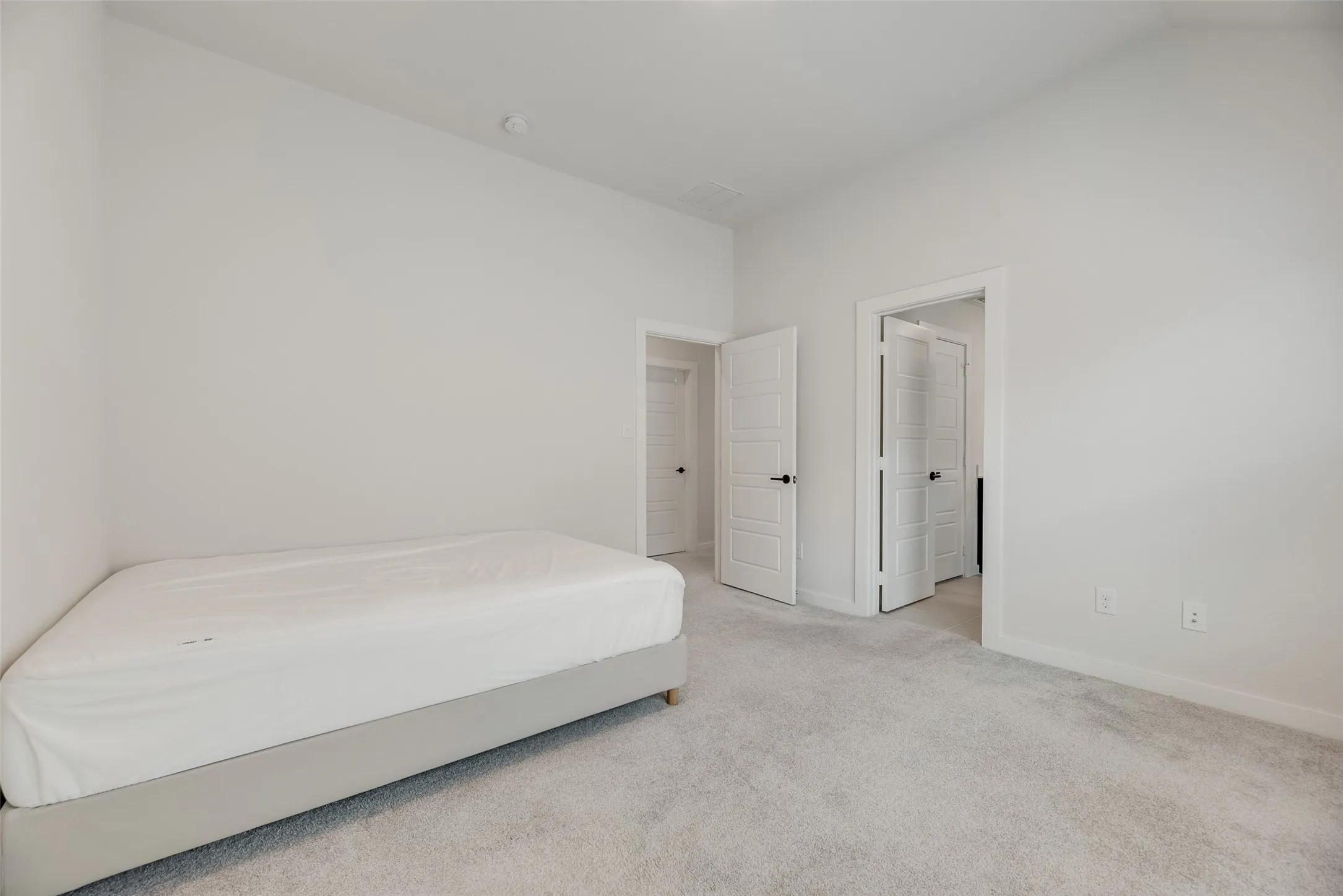 Carpeted bedroom featuring multiple doorways, crisp white walls, and bright overhead lighting