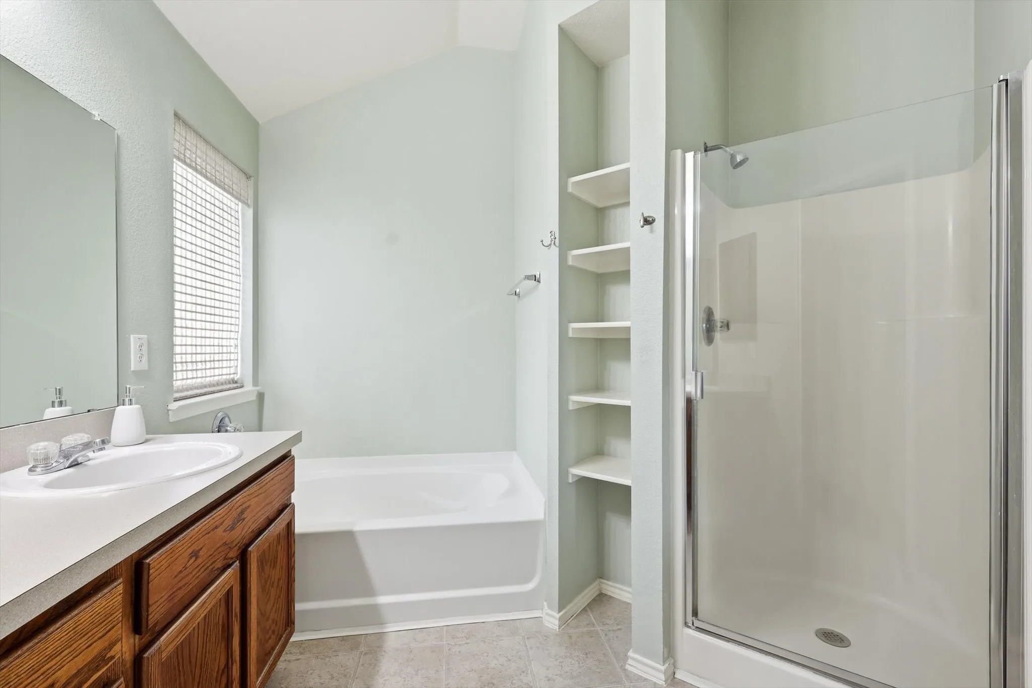 Bathroom featuring a single vanity with wood cabinetry, a built-in tub, a separate glass-enclosed shower, and integrated shelving