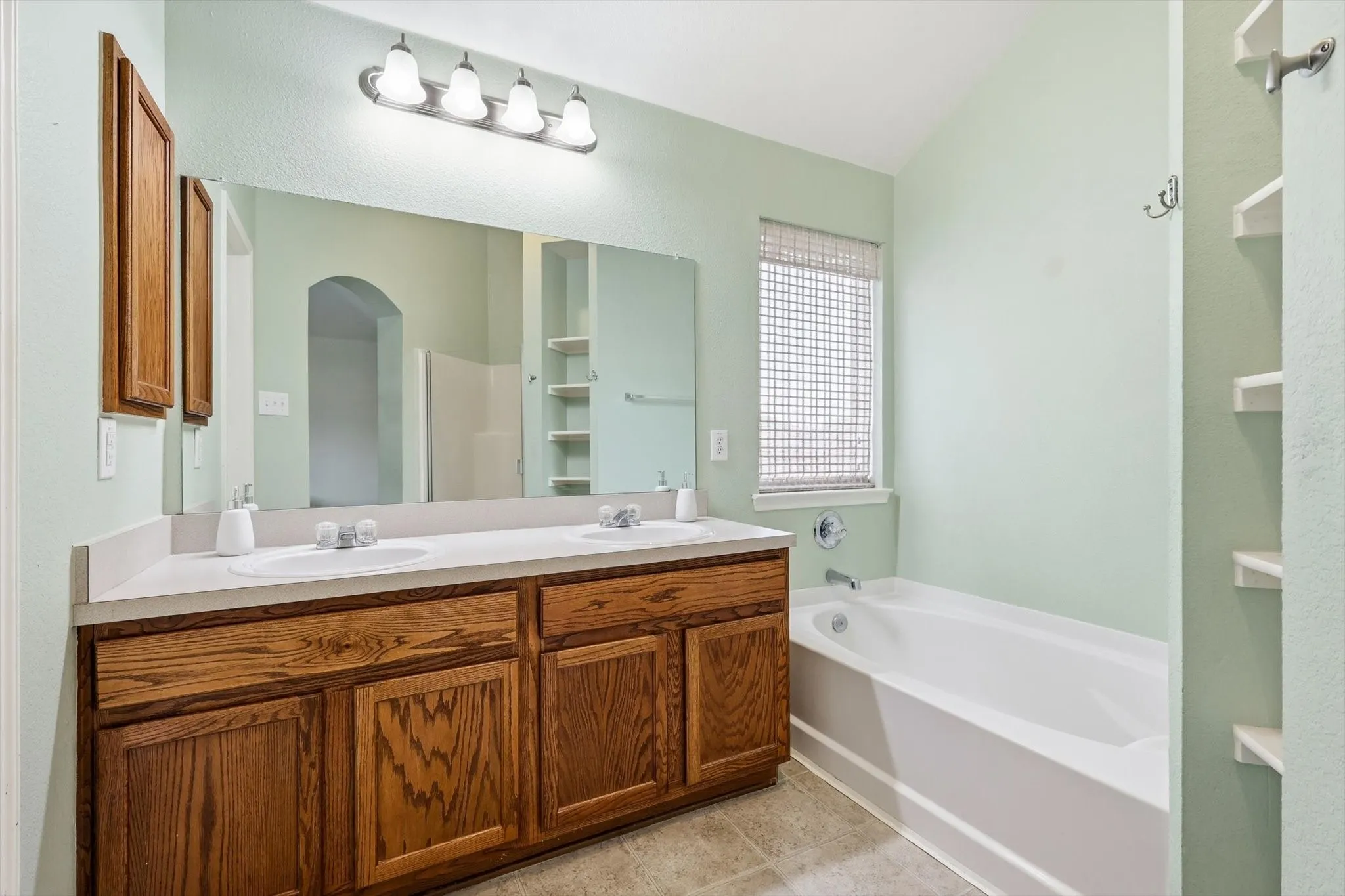 Bathroom featuring a double vanity with wood cabinetry, a large mirror, a four-light fixture, and an integrated bathtub with an overhead window