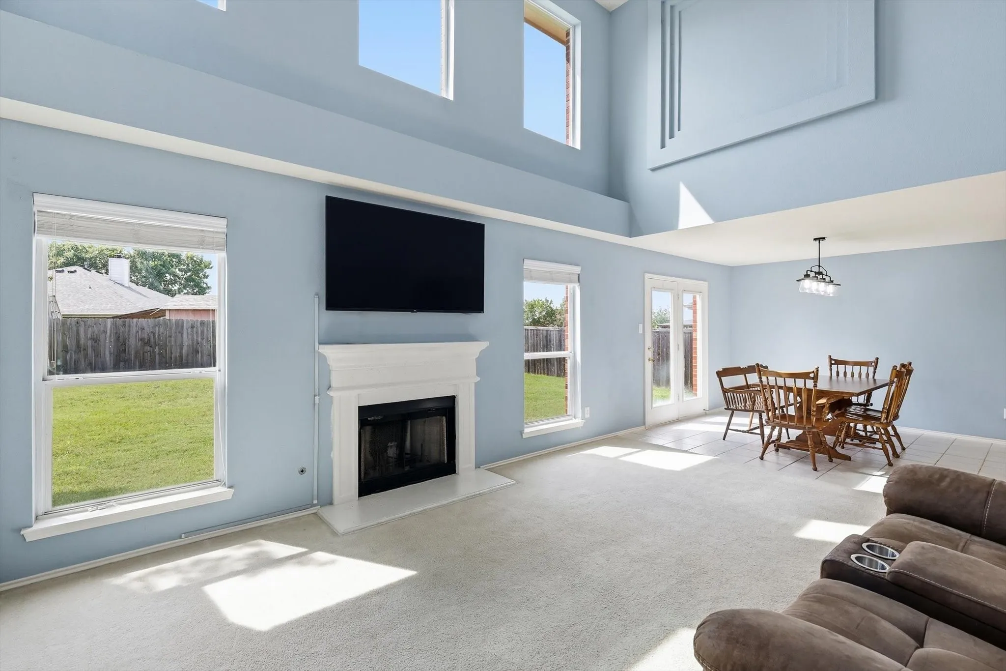 Living area featuring a fireplace with a white mantel, multiple large windows, and high ceilings