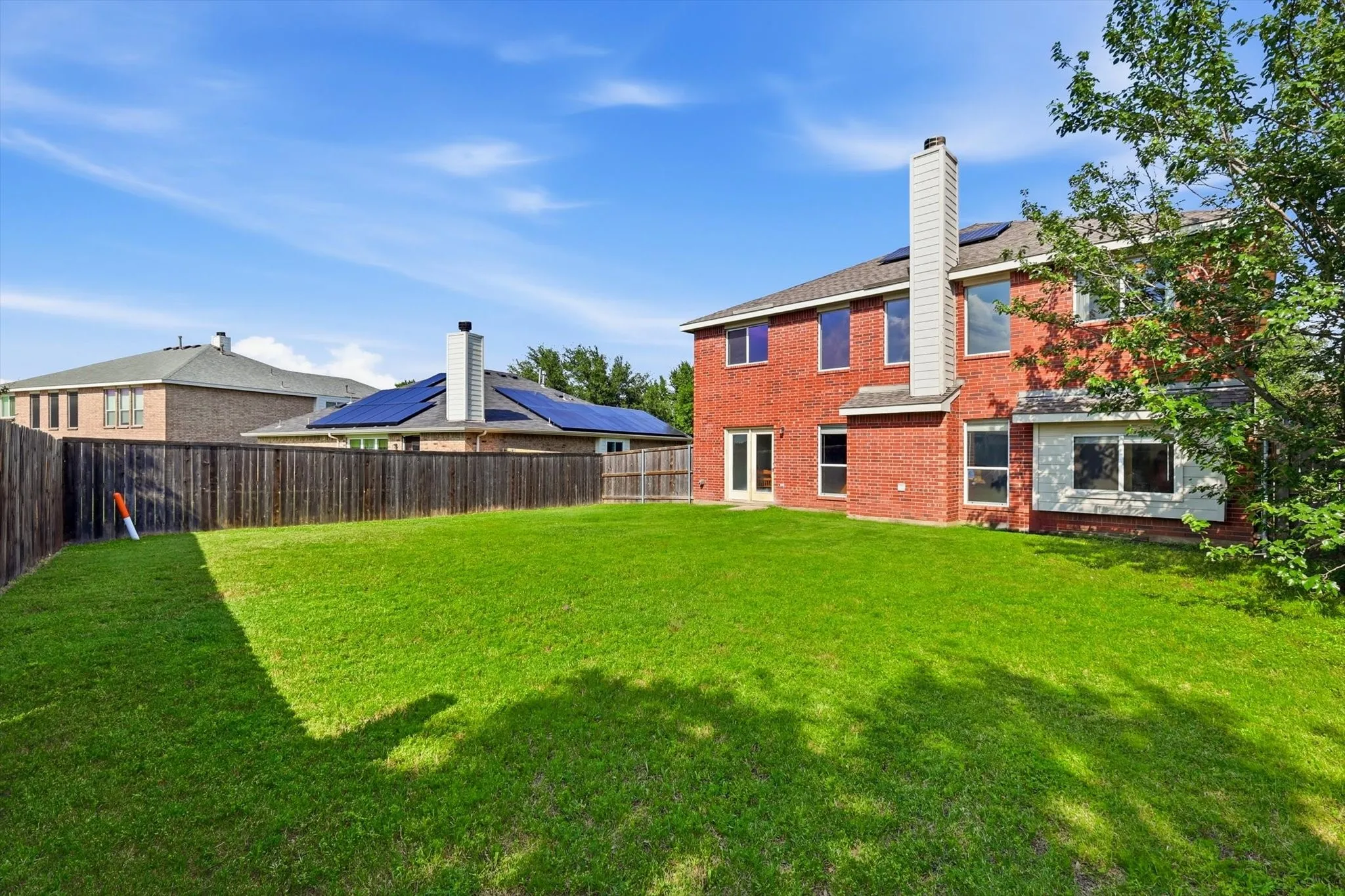 Spacious backyard featuring a large lawn, full brick exterior, a tall chimney, and multiple windows